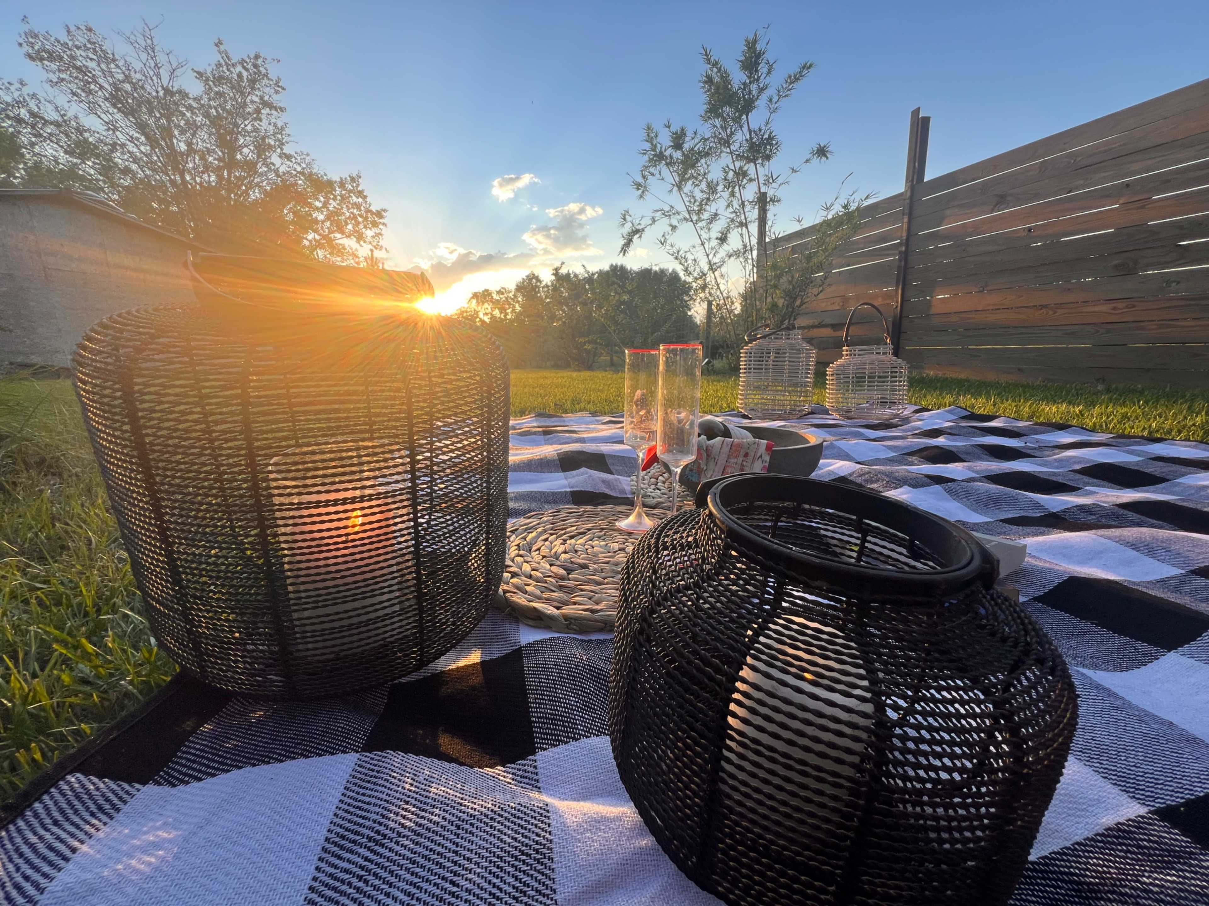 The image depicts a picnic setting on a checkered blanket with lanterns and glasses, bathed in the warm glow of a setting sun.
