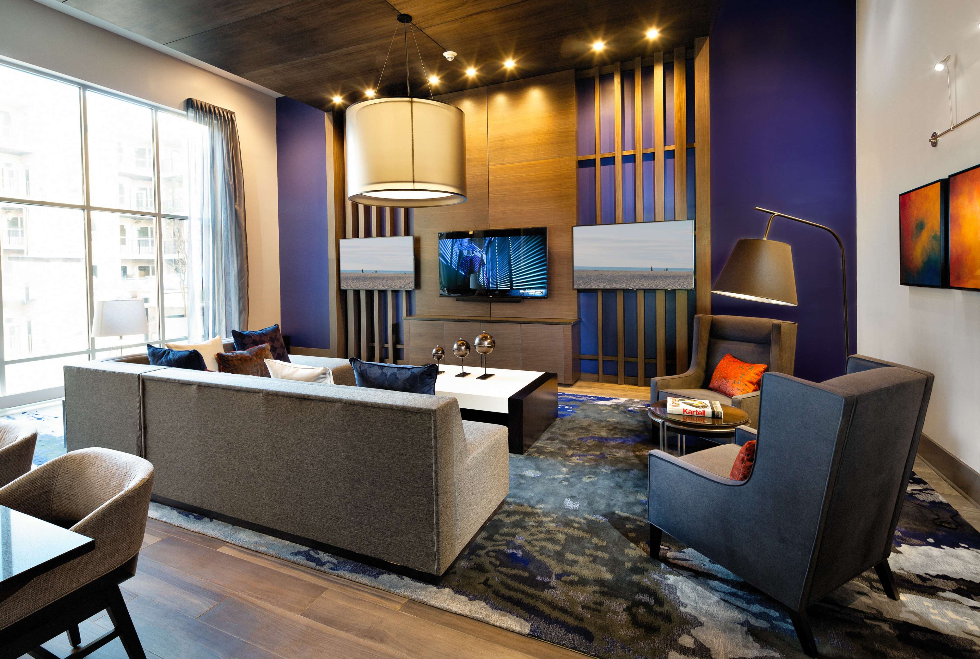 A modern living room with a large window, a sectional couch, a coffee table, a wall-mounted television, and decorative artworks.