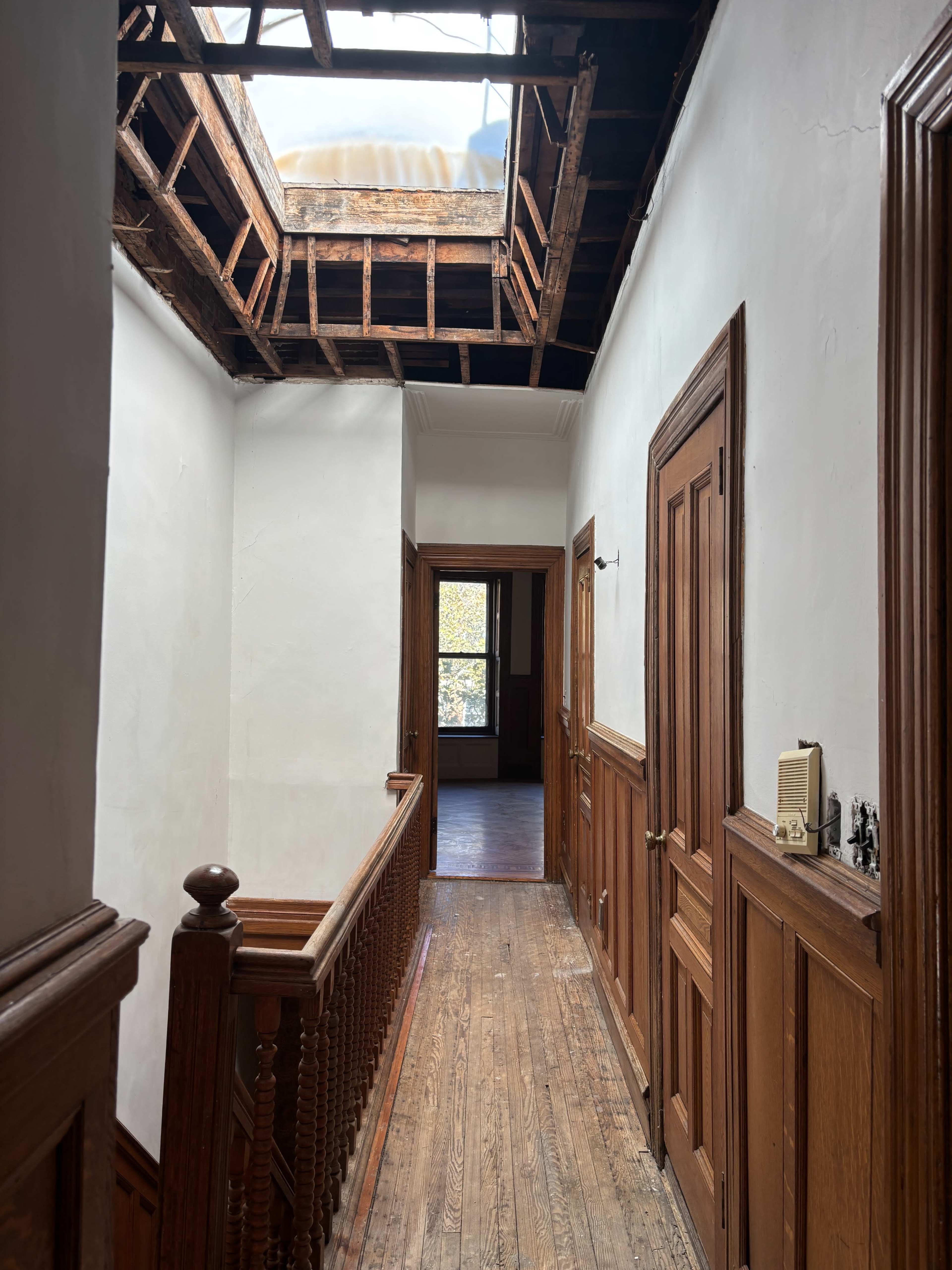 A hallway with wooden railings and doors leading to adjacent rooms, featuring an open skylight that exposes the rafters above.