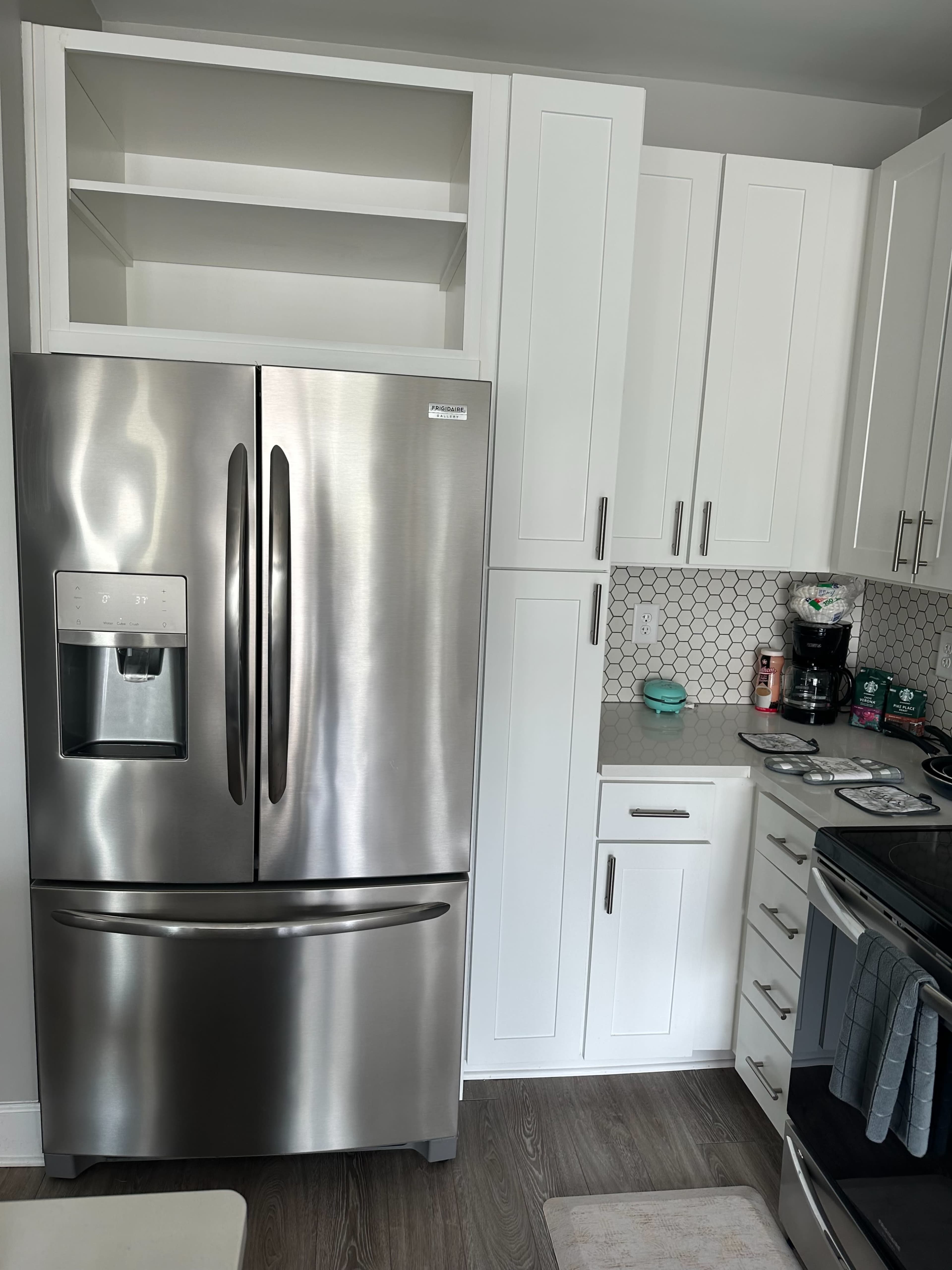 A modern kitchen featuring a stainless steel refrigerator, white cabinetry, and a countertop with small appliances and a backsplash of hexagonal tiles.