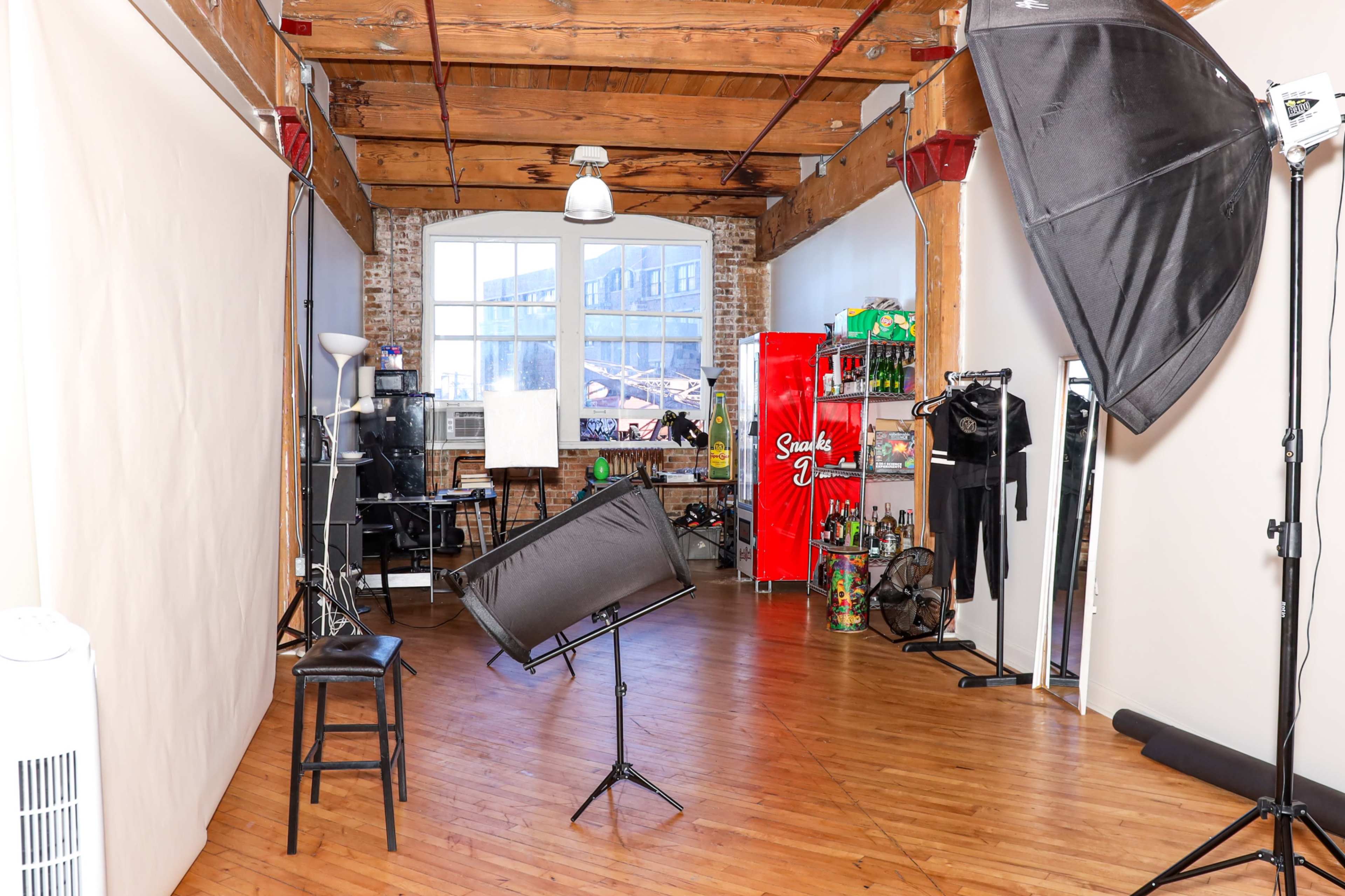 The image shows a photography studio featuring a large backdrop, lighting equipment, and various props and accessories on display.
