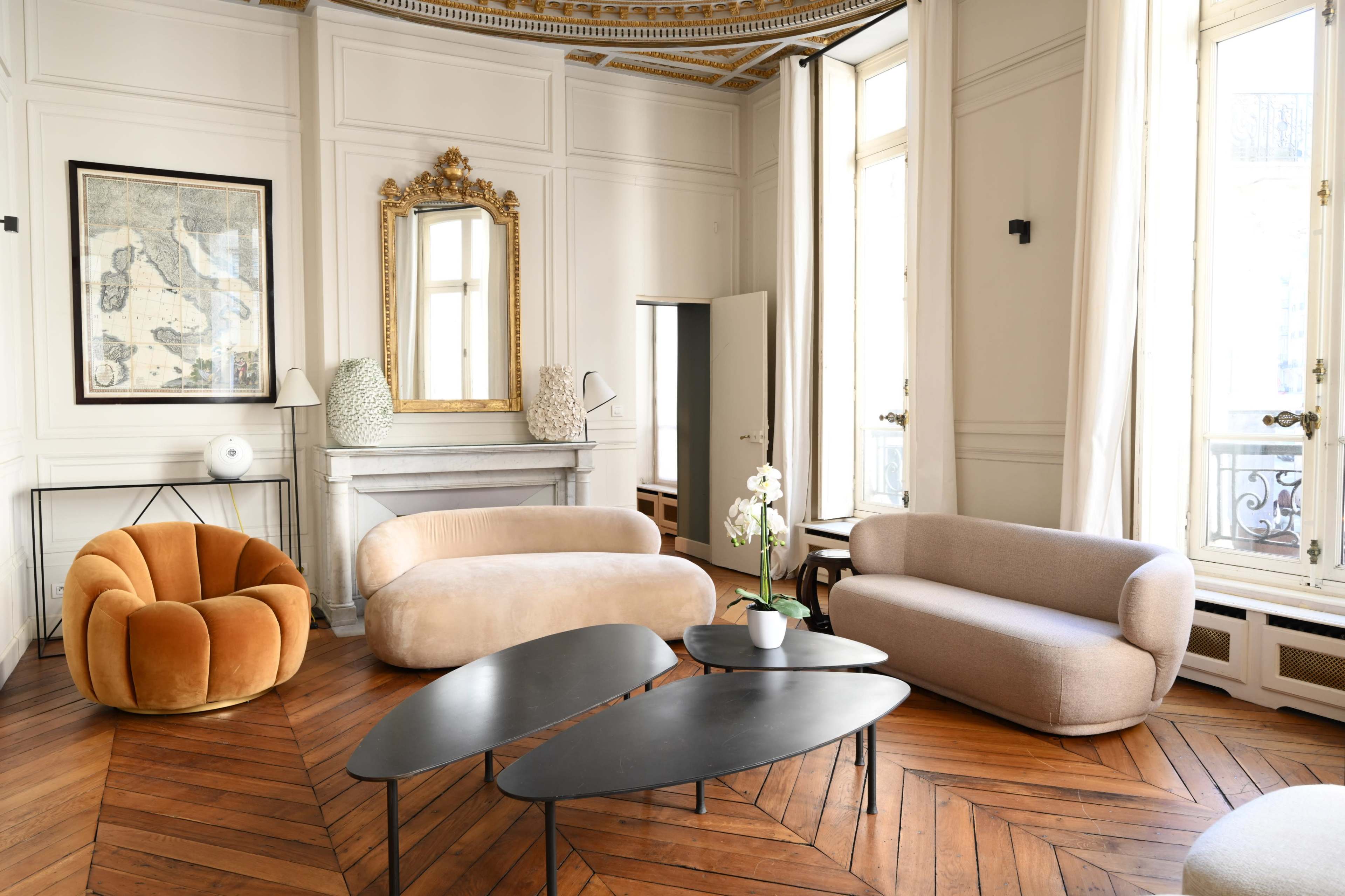 The room features a stylish arrangement of contemporary furniture, including a plush orange chair, a beige sofa, and sleek black coffee tables, all set against a backdrop of elegant architectural details.