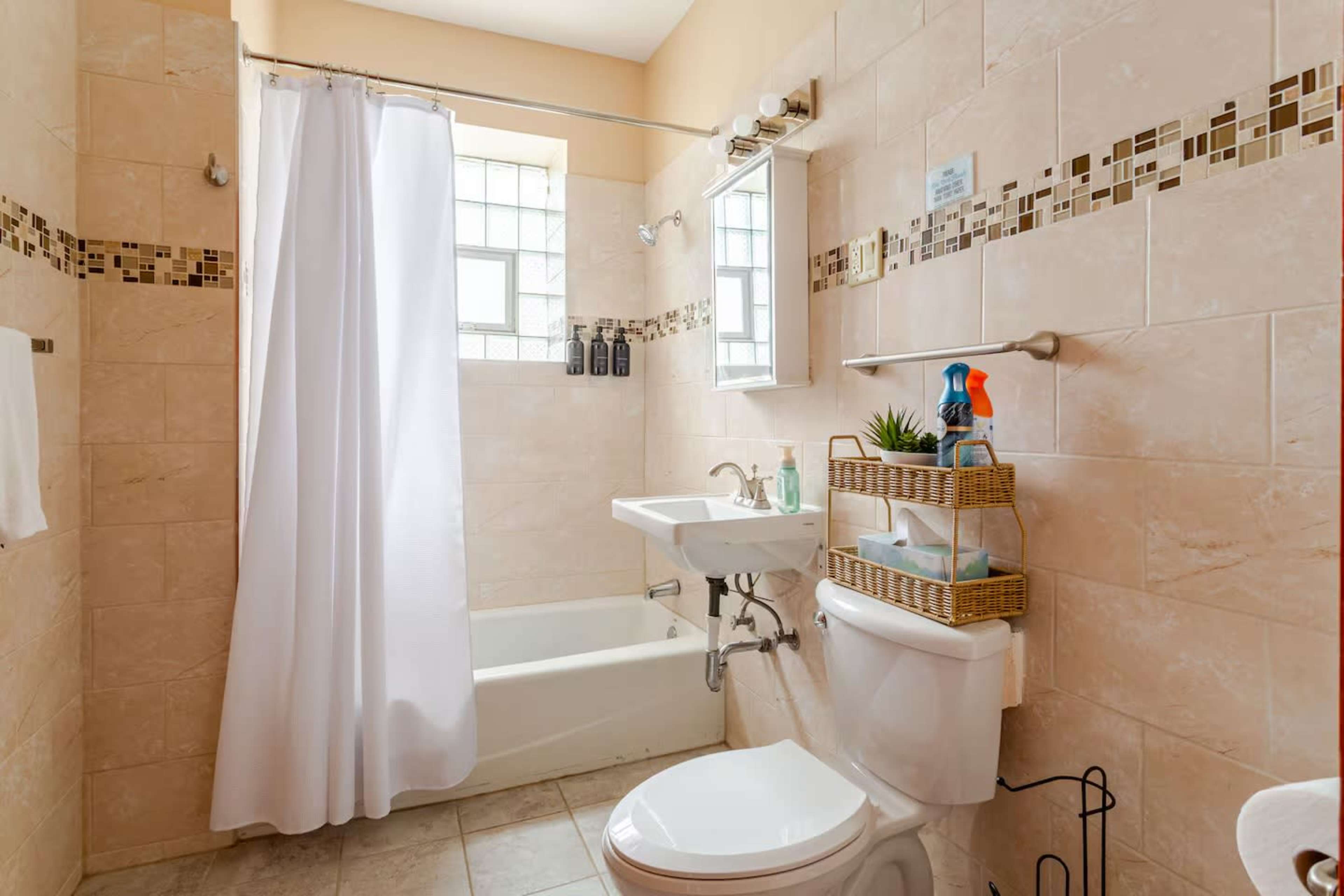 The bathroom features a bathtub with a shower curtain, a sink, a toilet, and a decorative shelf with cleaning supplies and plants.