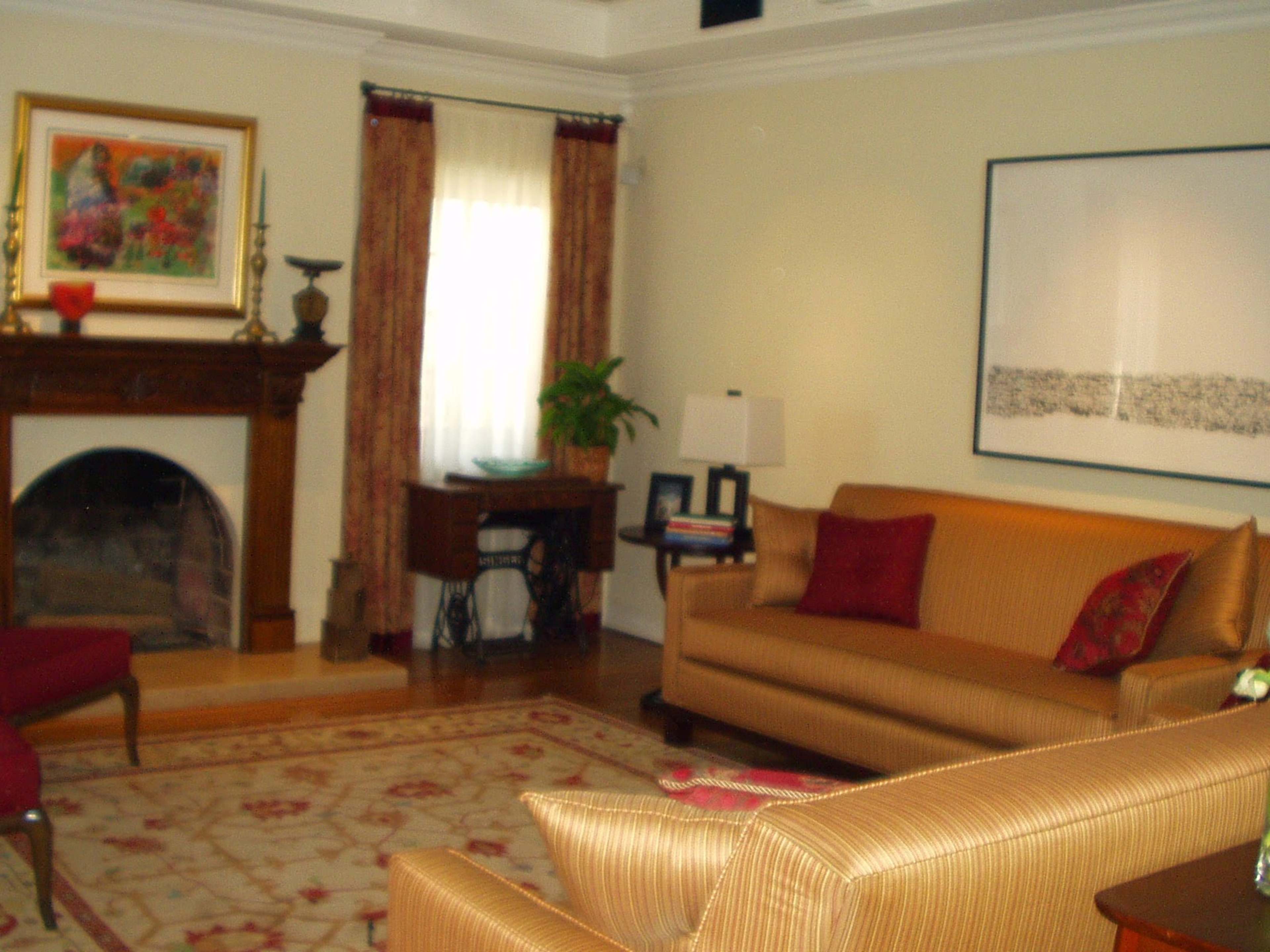 The image shows a living room featuring a fireplace, two sofas, a decorative rug, and large windows with curtains.
