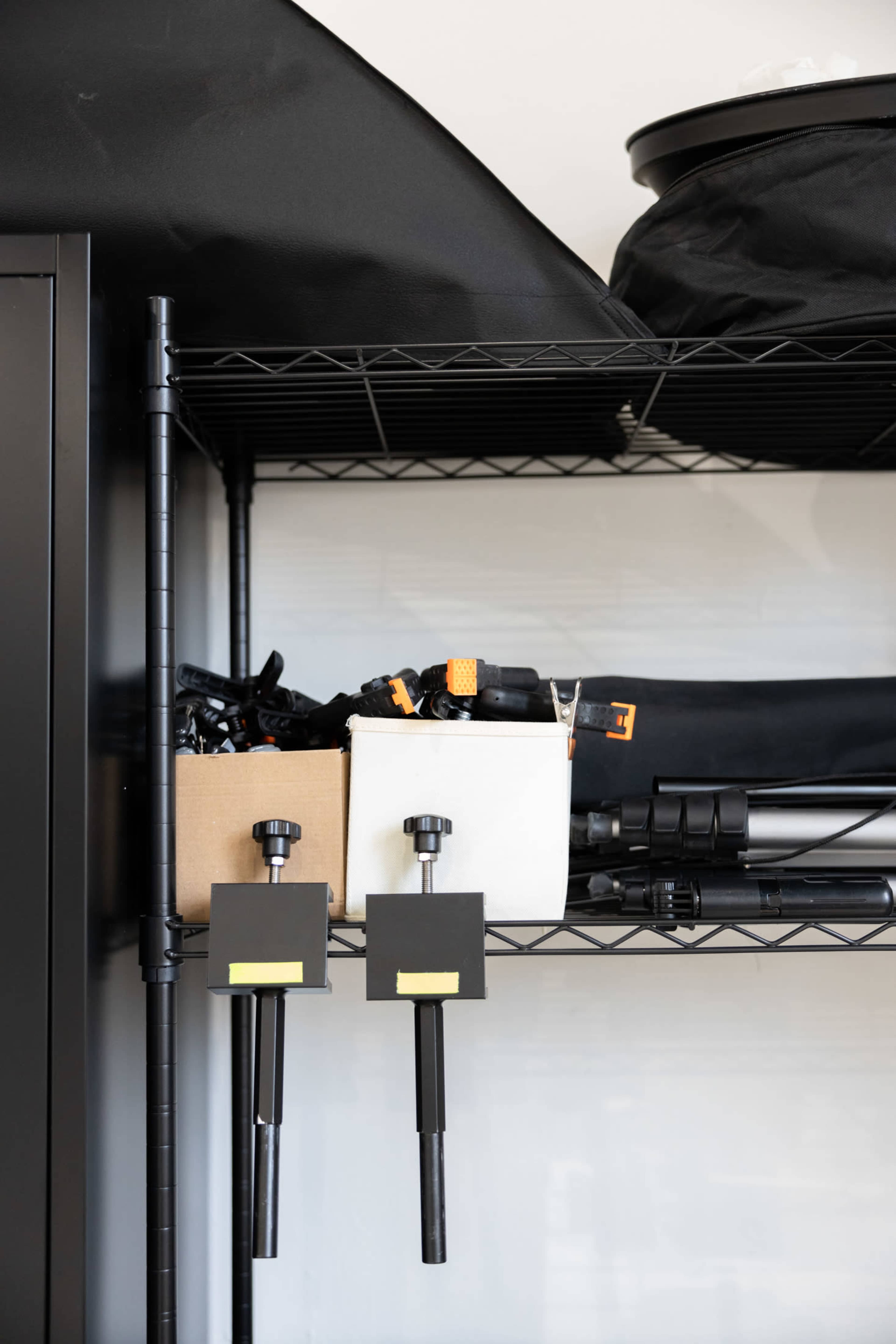 A metal shelving unit containing various photography equipment, including light stands and accessories, arranged neatly on the shelves.
