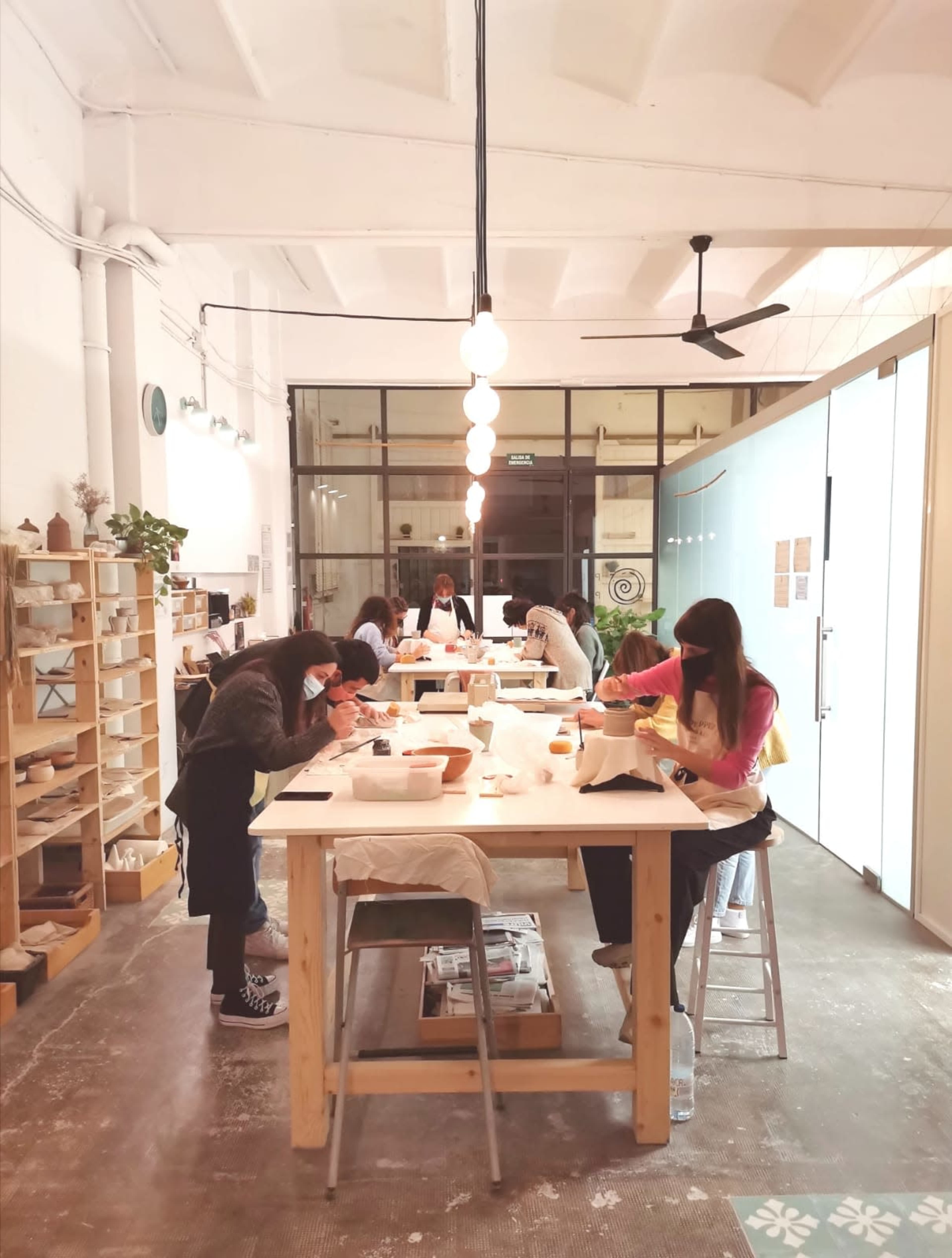 A group of individuals is engaged in pottery crafting at a long table in a bright, minimalist studio.