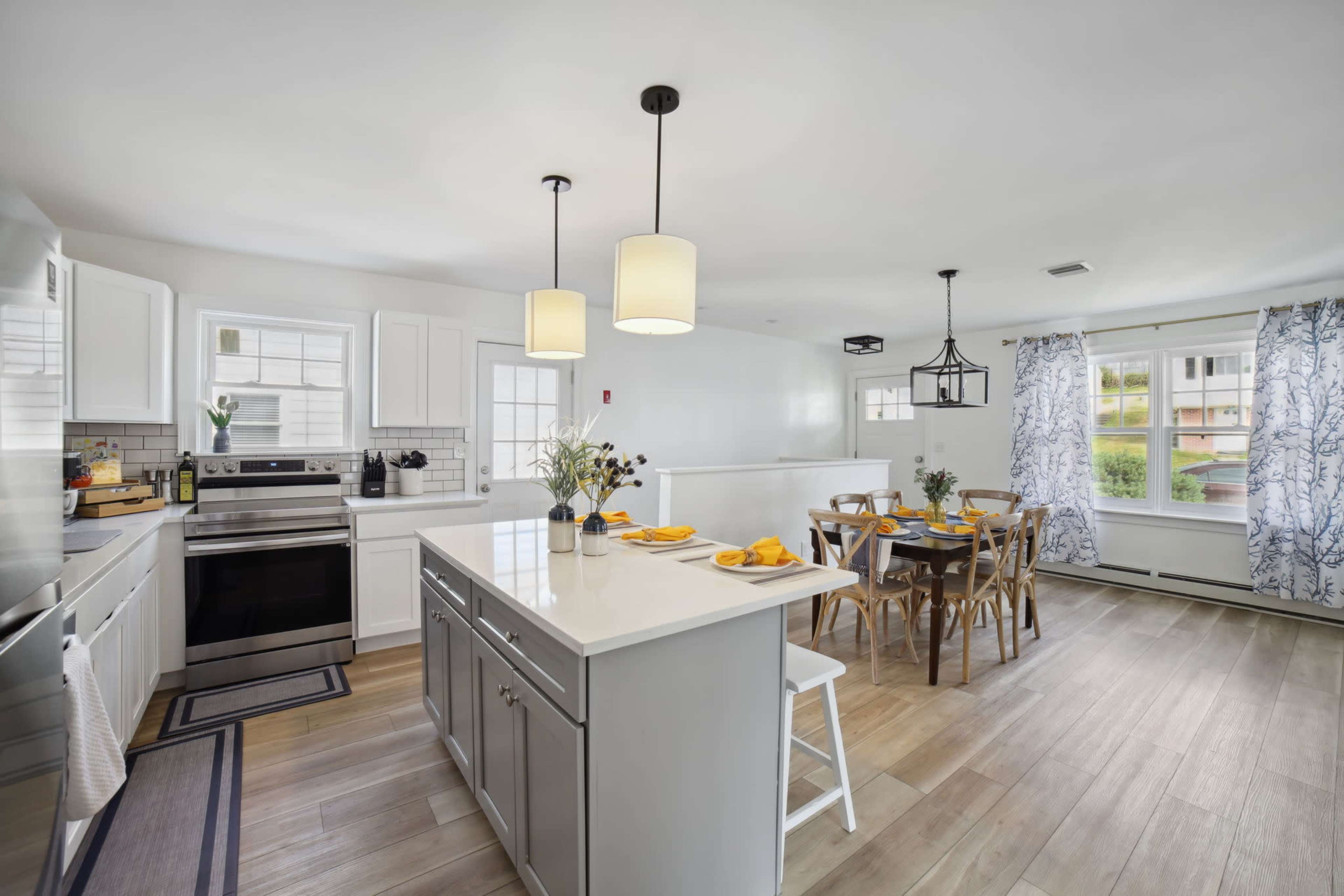 A modern kitchen with white cabinets and a central island, featuring a dining area nearby with a wooden table and chairs.