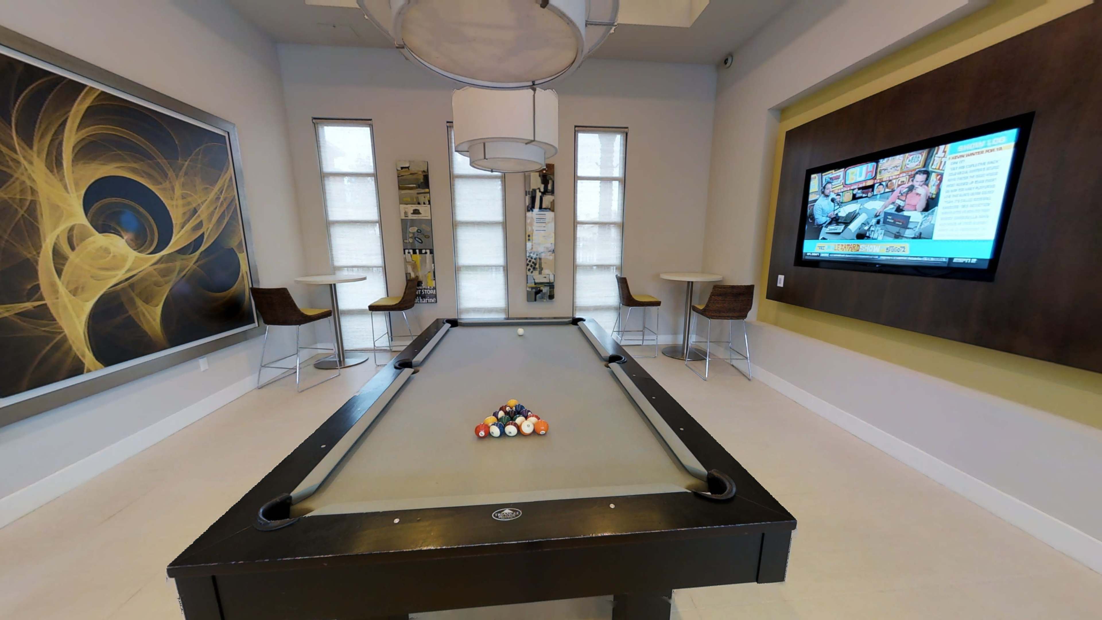 A game room featuring a pool table with a full rack of balls, two bar-style tables, and a television mounted on the wall.