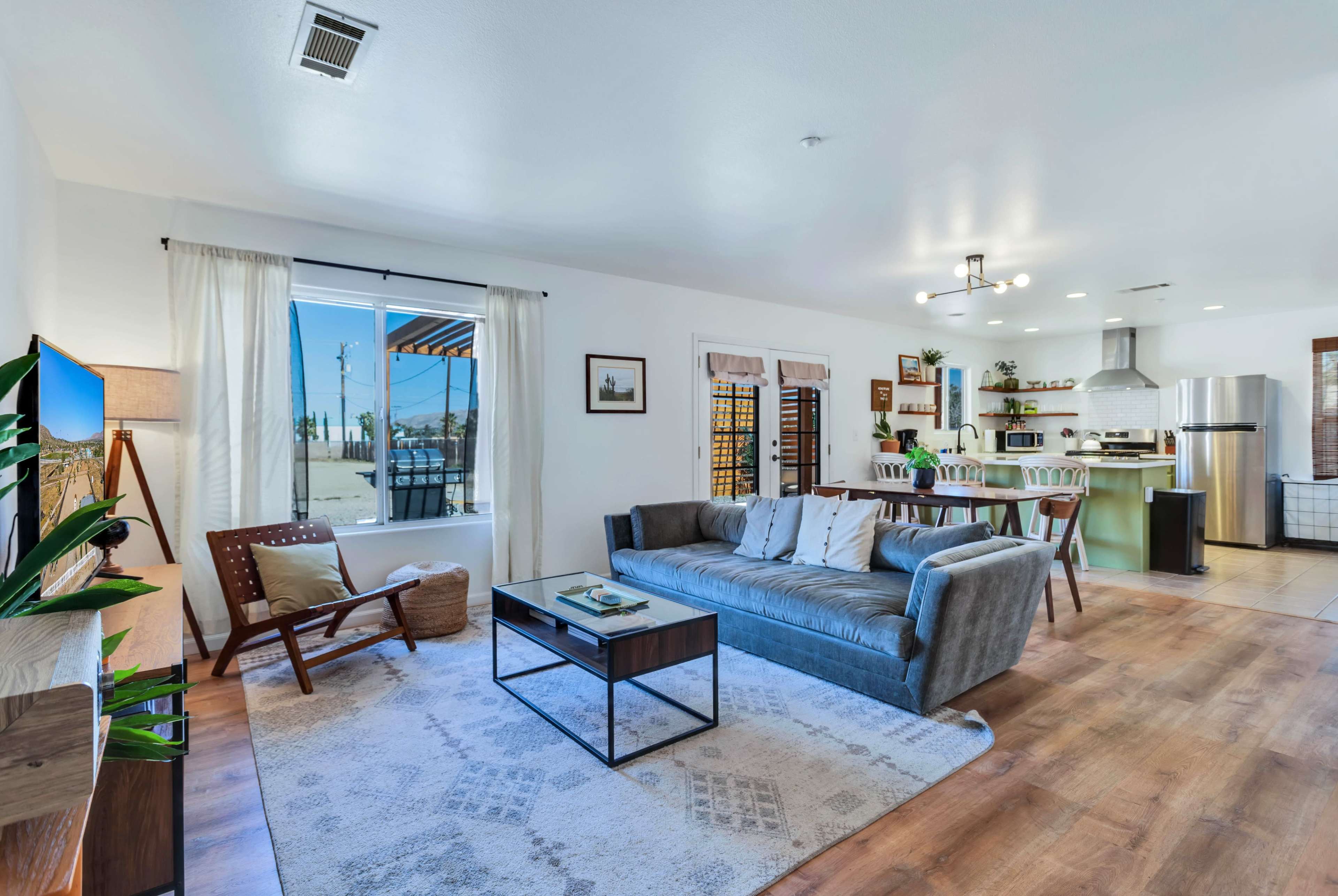 A modern, open living space with a gray sofa, a coffee table, and a view of a landscaped outdoor area through a large window.