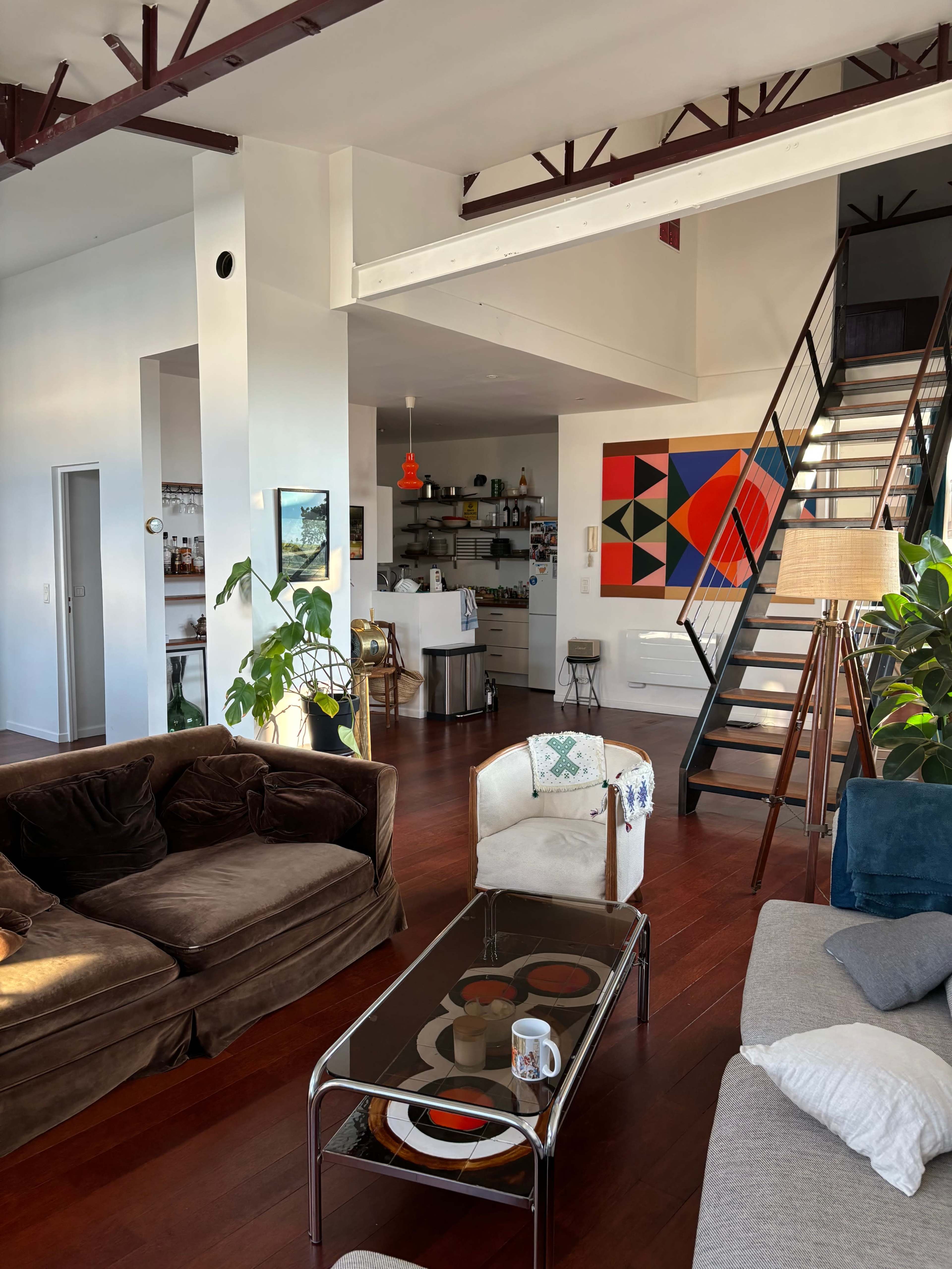 The image shows a spacious living area with a staircase, modern furniture, and colorful artwork on the wall.