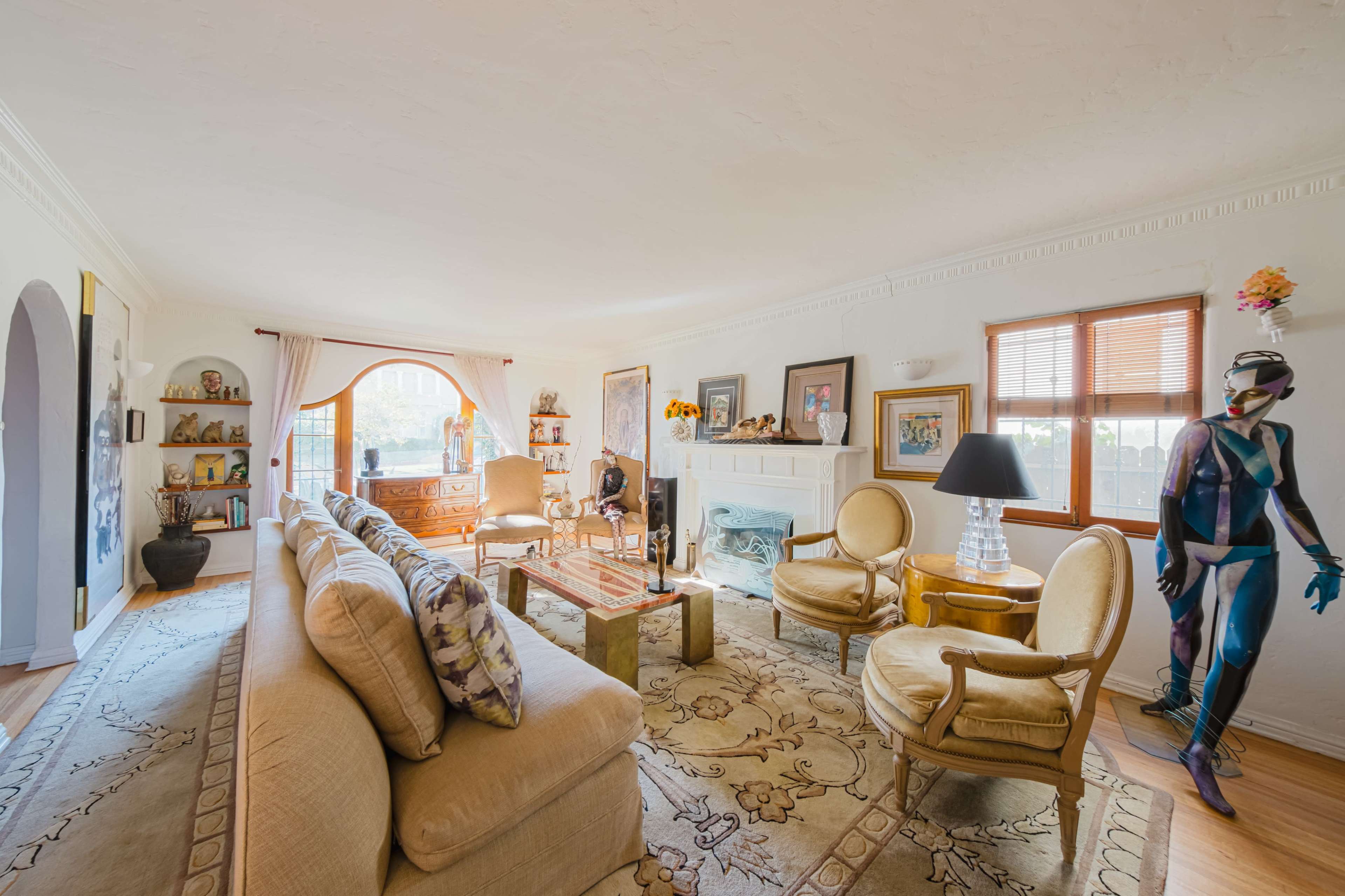 The living room features a beige sofa, two yellow armchairs, a wooden coffee table, and a decorative corner with a window and various artworks.