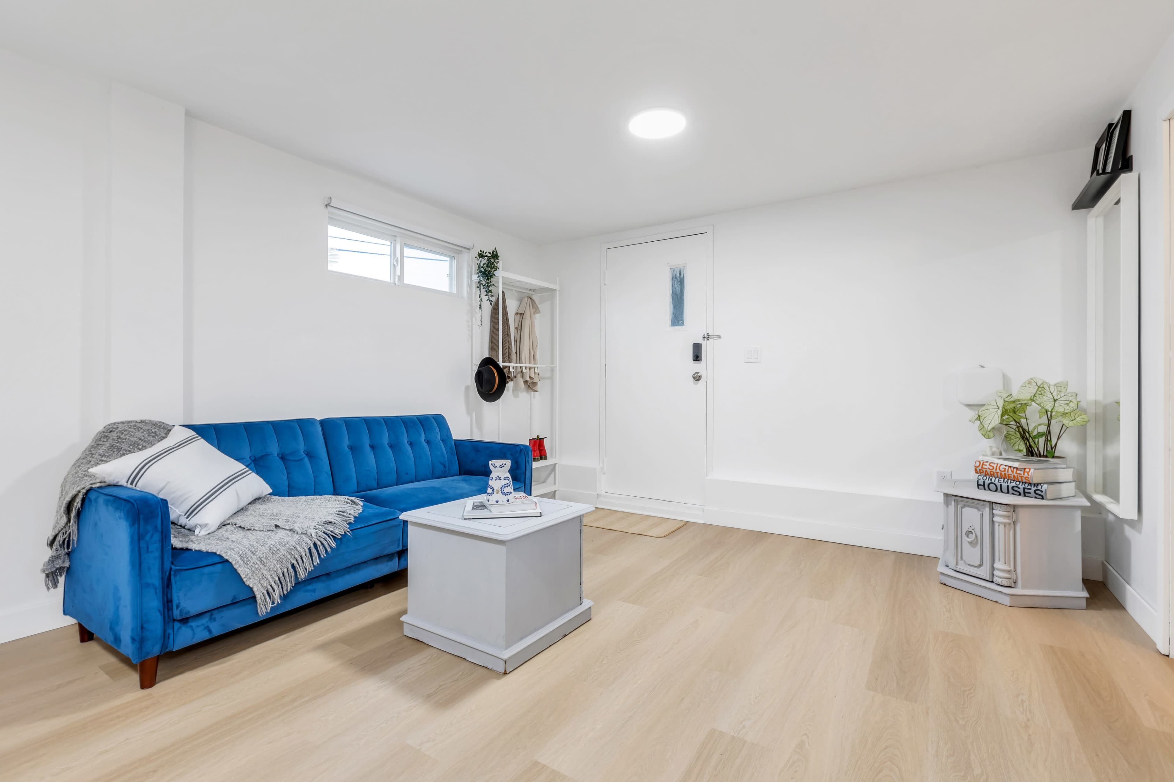 A bright, modern living space featuring a blue couch, a small gray coffee table, and a door leading outside.