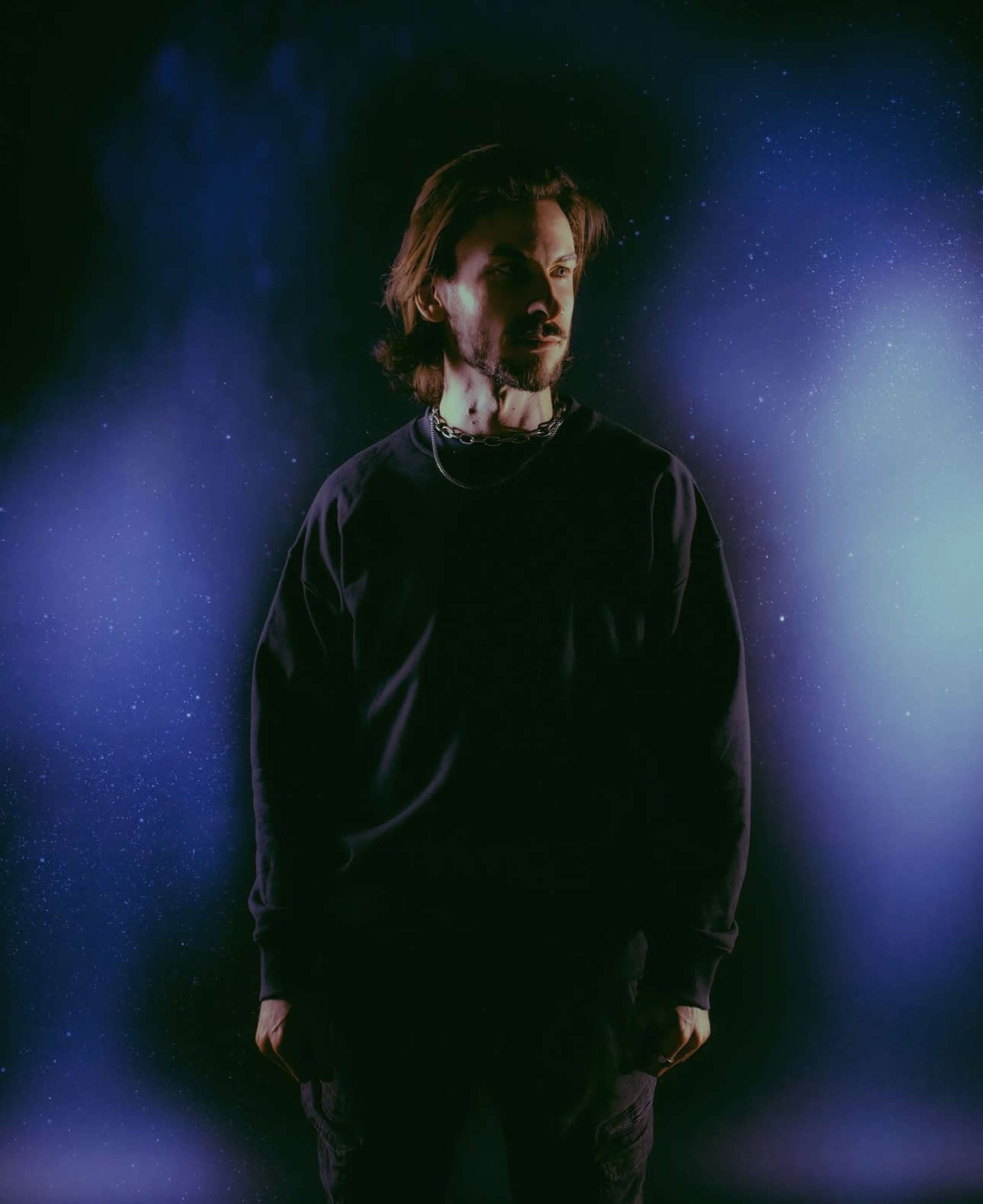 A man stands confidently against a dark, cosmic backdrop filled with subtle star-like specks.