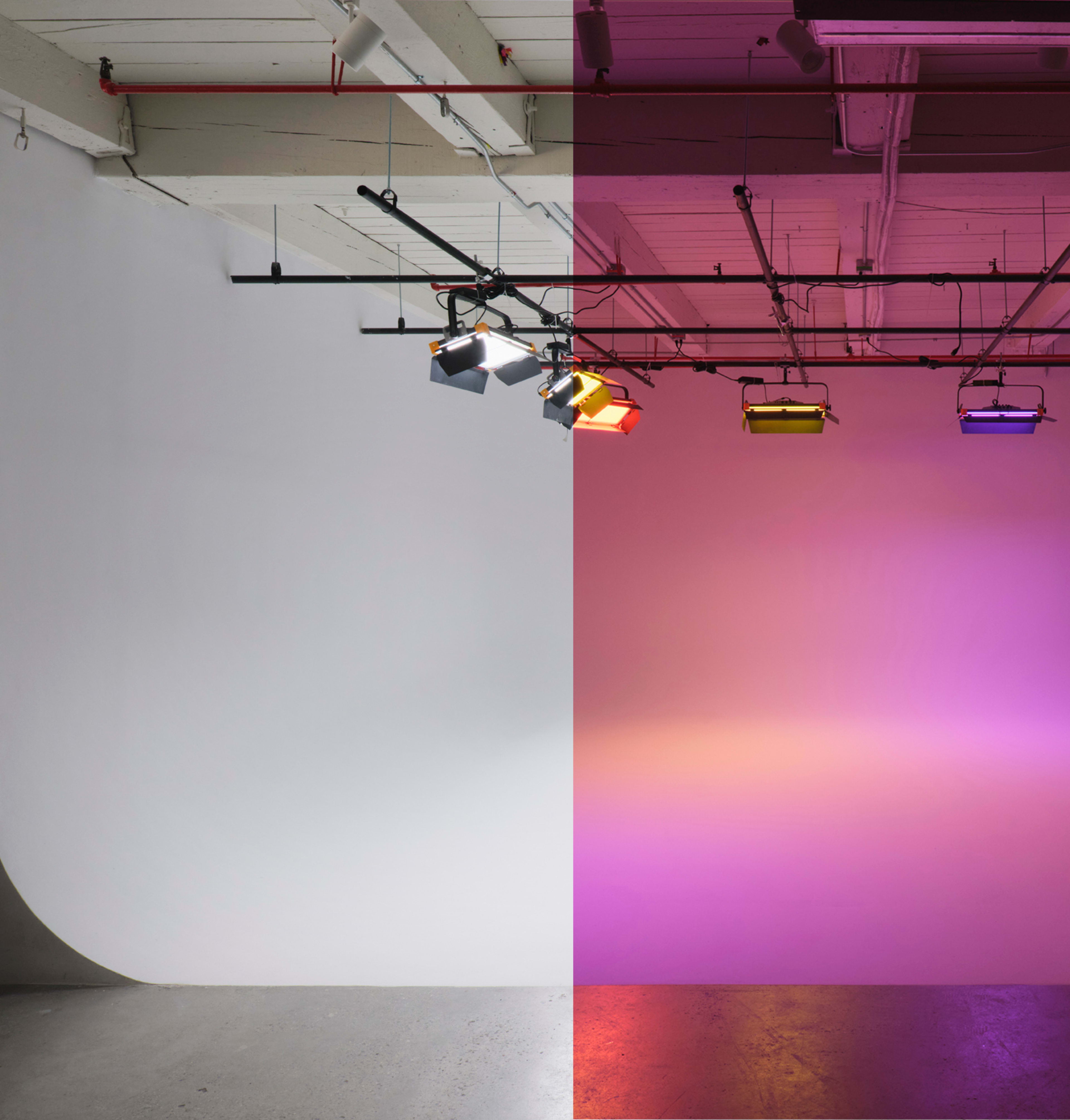 The image shows a studio space divided between a plain white wall on the left and a brightly lit purple gradient wall on the right, illuminated by stage lights.