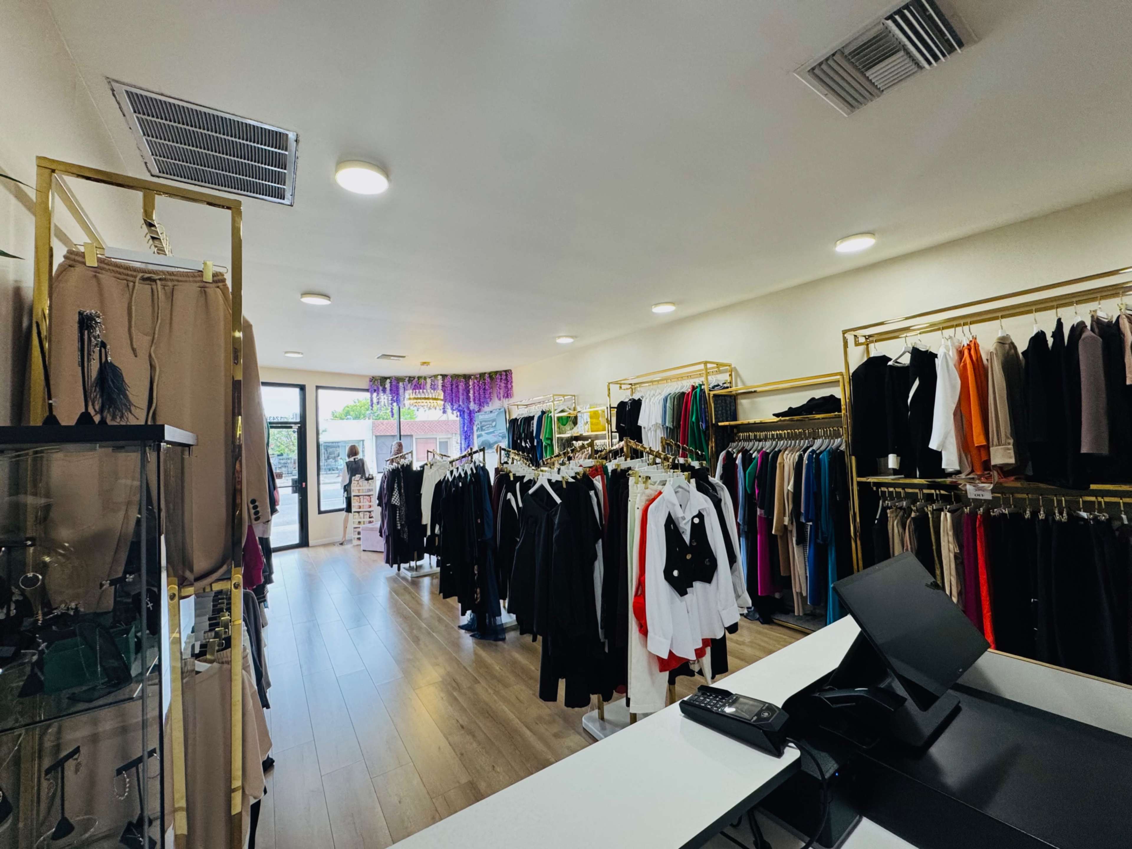 The image shows an interior of a clothing store with racks of apparel and a cash register near the front entrance.