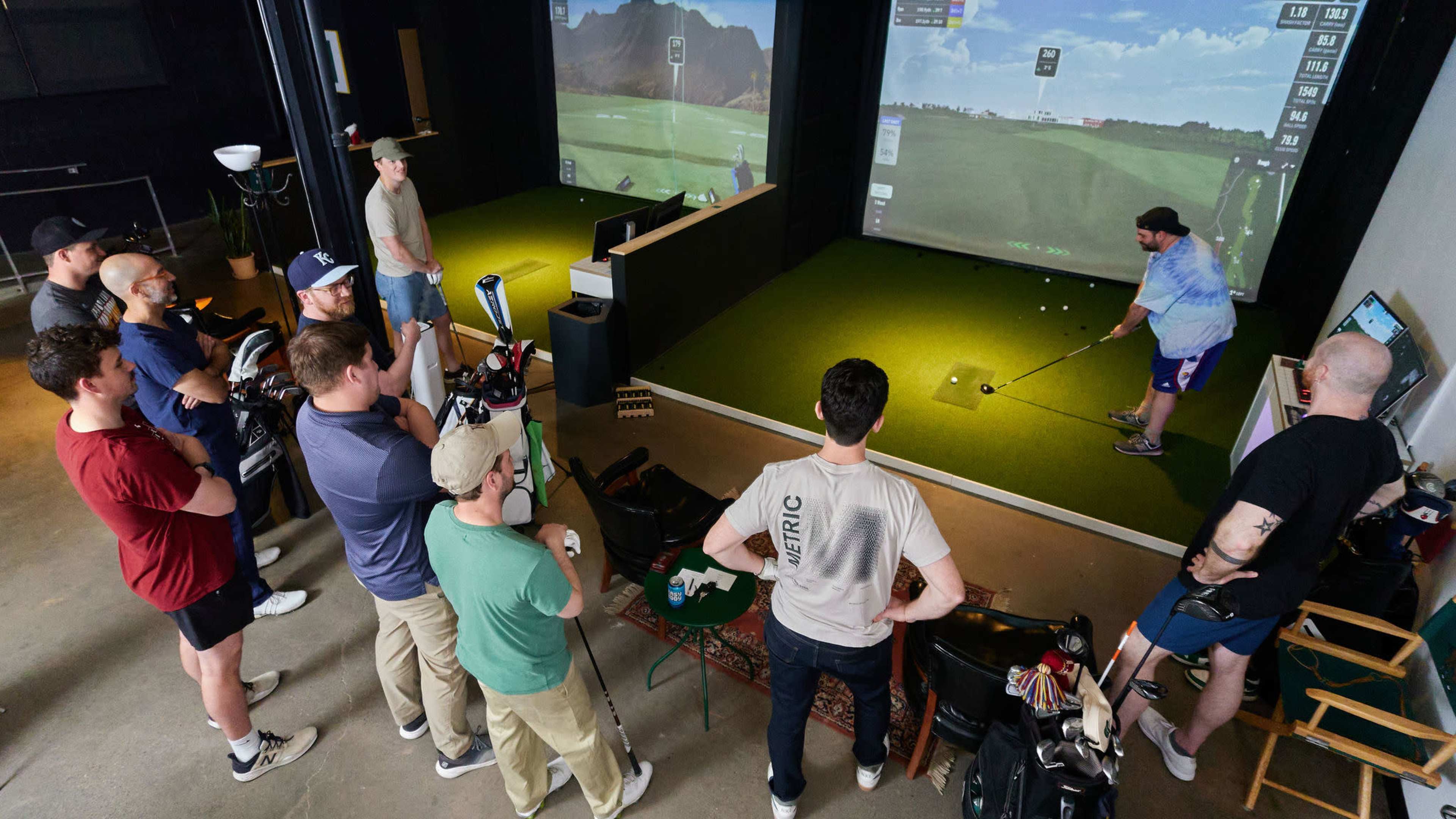 A group of people watches as one individual prepares to swing a golf club in a simulated golfing environment.