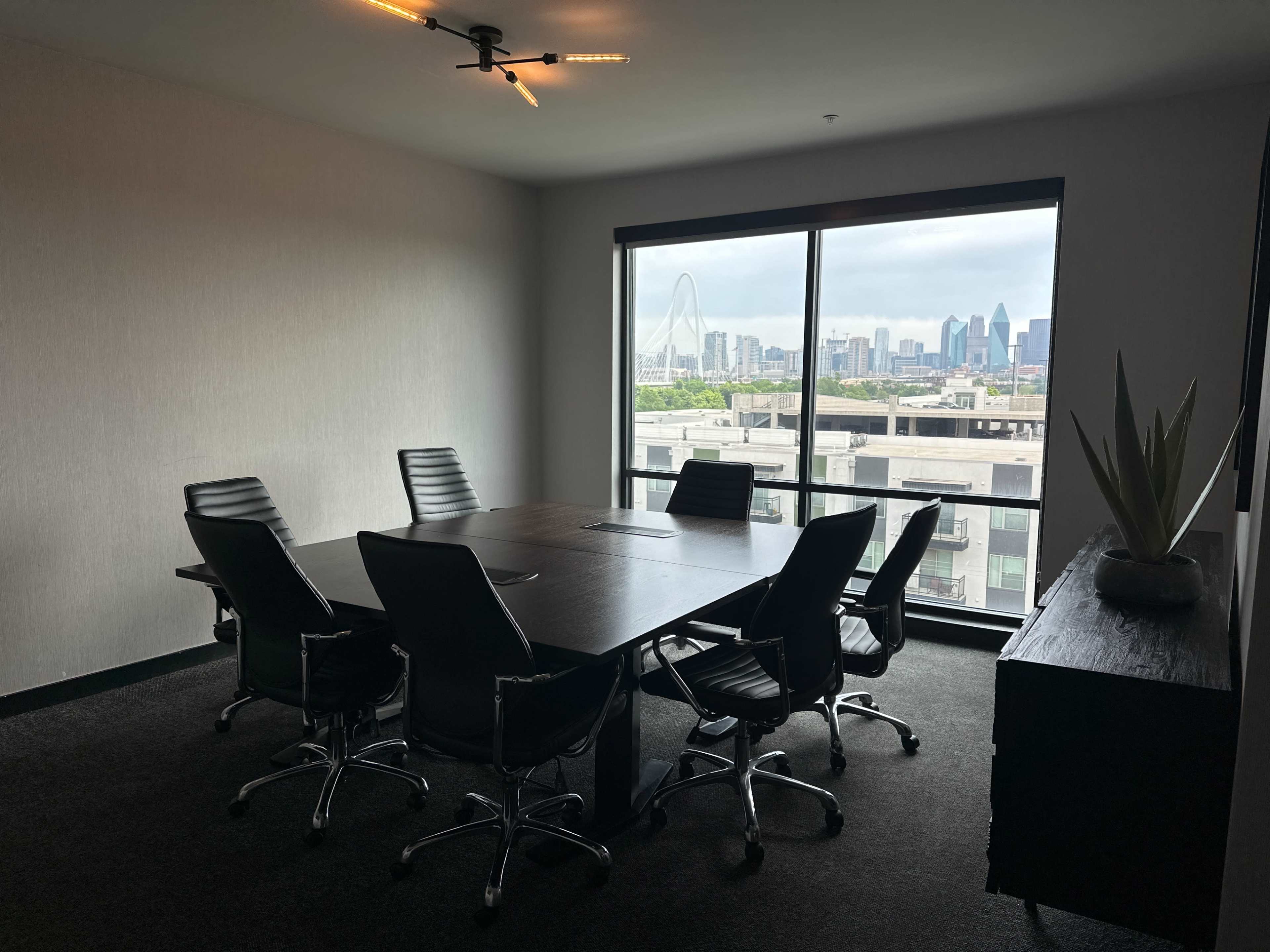 A conference room features a large table surrounded by six chairs, with a view of a city skyline visible through a large window.