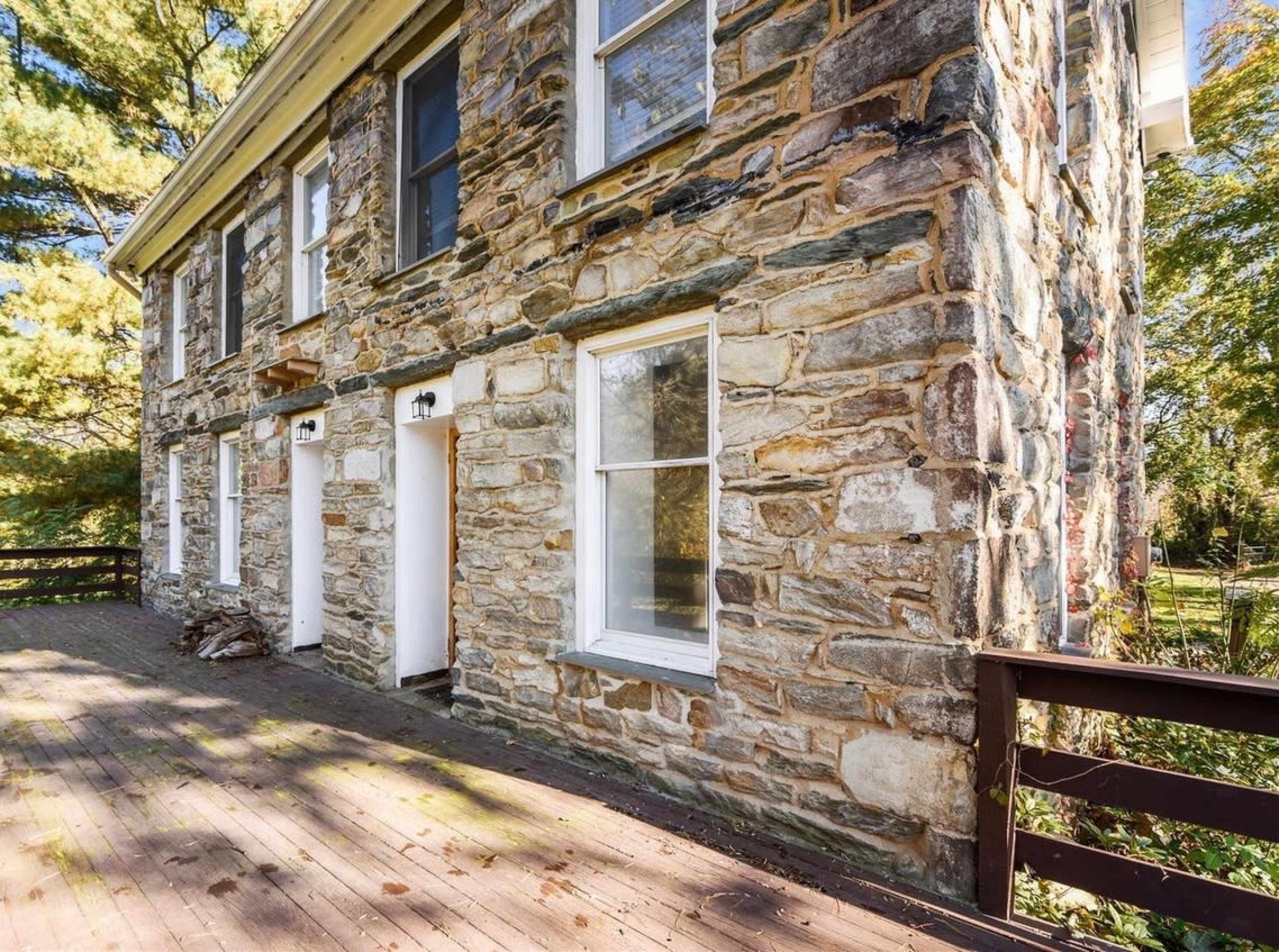 A stone building with two white doors and a wooden deck in front, surrounded by trees.