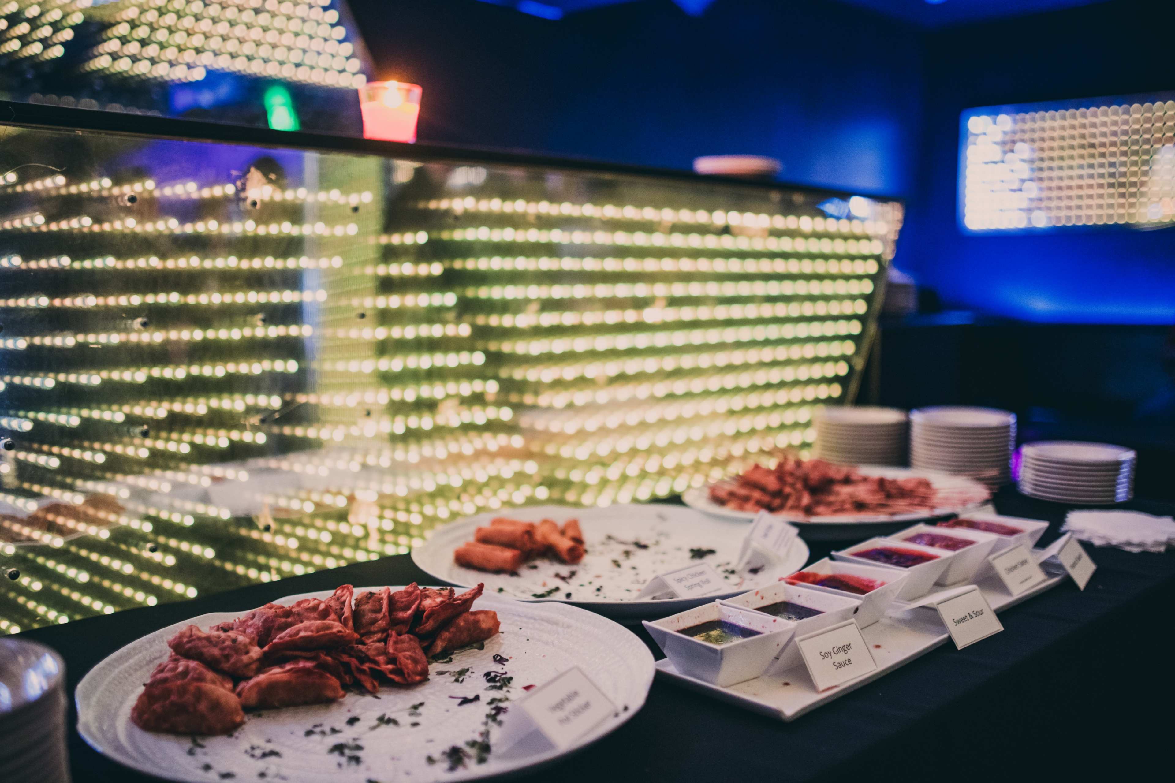A buffet display features various plates of food and condiments, illuminated by a backdrop of bright lights.