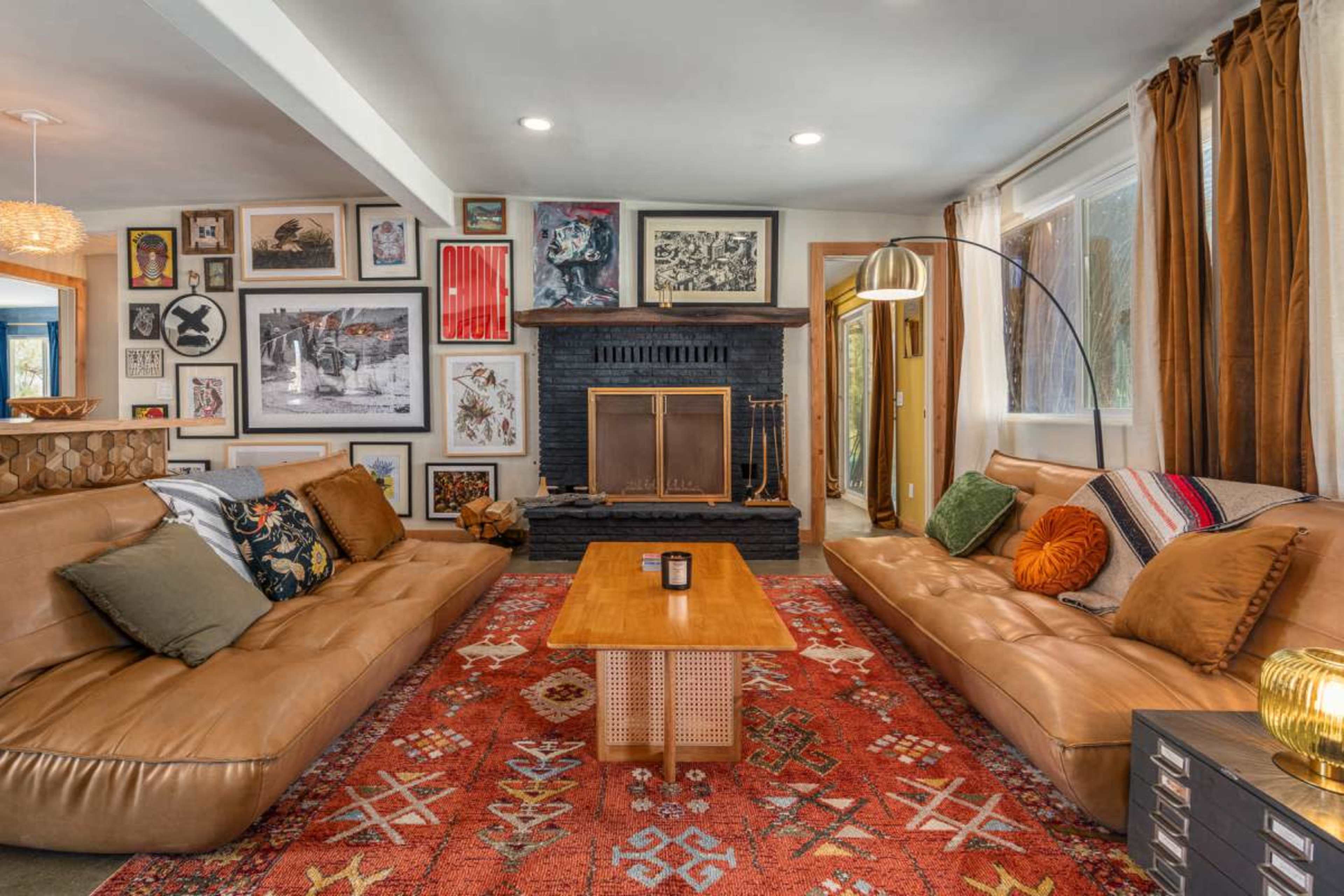 The living room features two leather sofas facing a wooden coffee table, with a fireplace and an array of framed artwork on the walls.