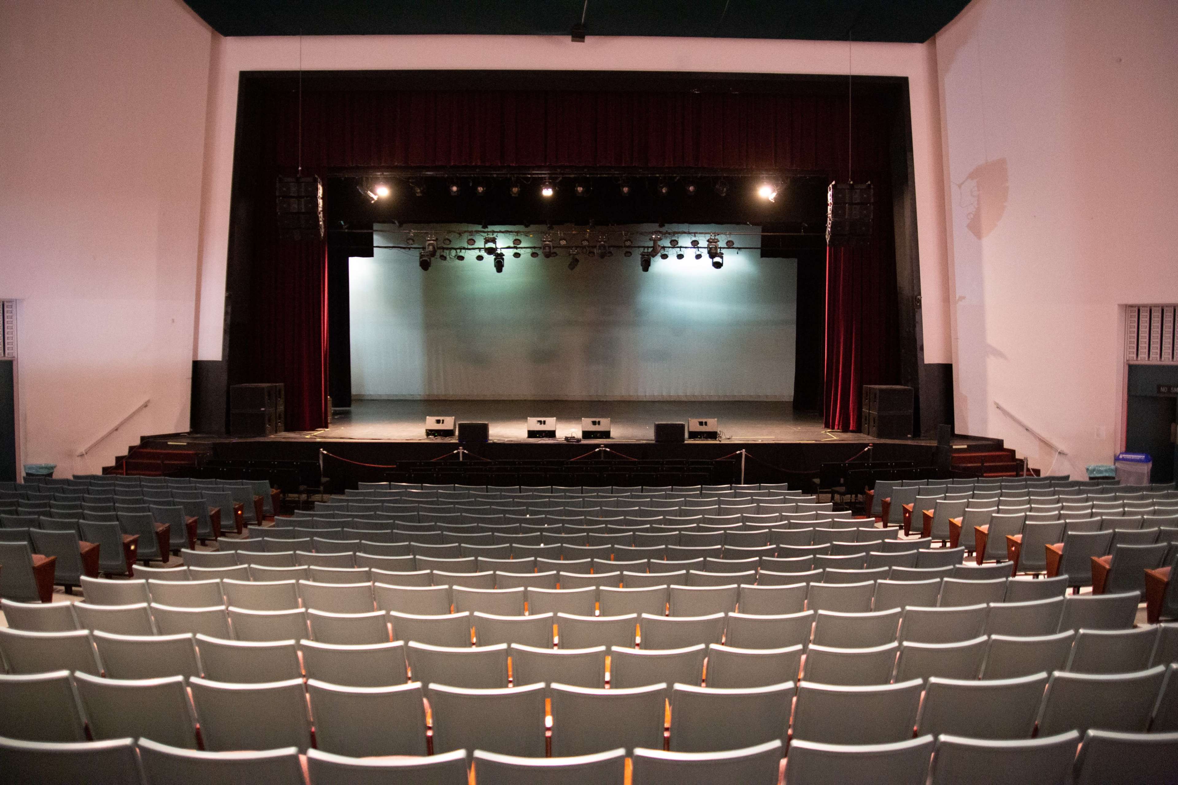 A large theater features a vacant seating area facing a stage with multiple speakers and lighting rigs.