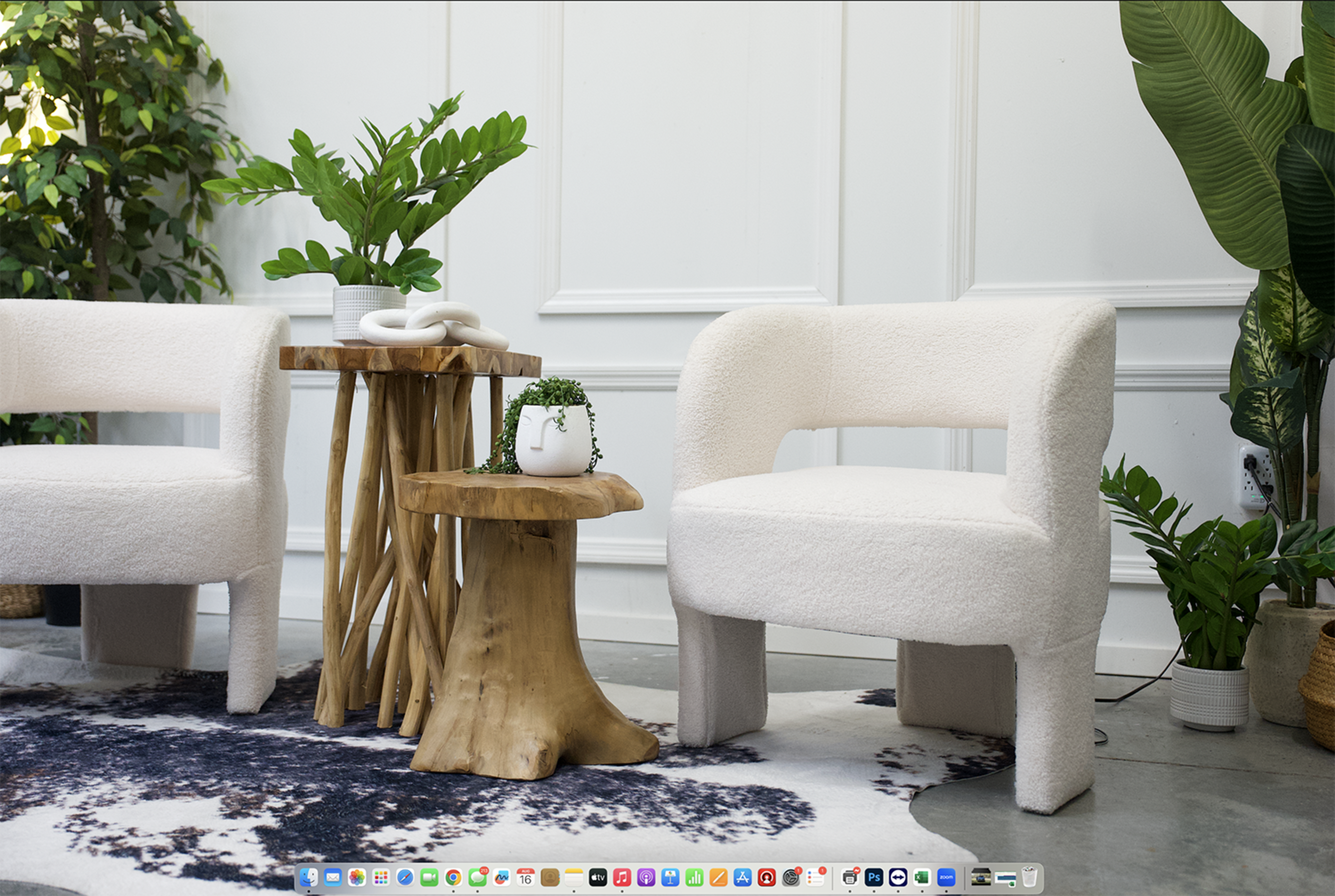 The image features two white armchairs next to a wooden side table, accompanied by decorative plants in a bright, modern interior space.