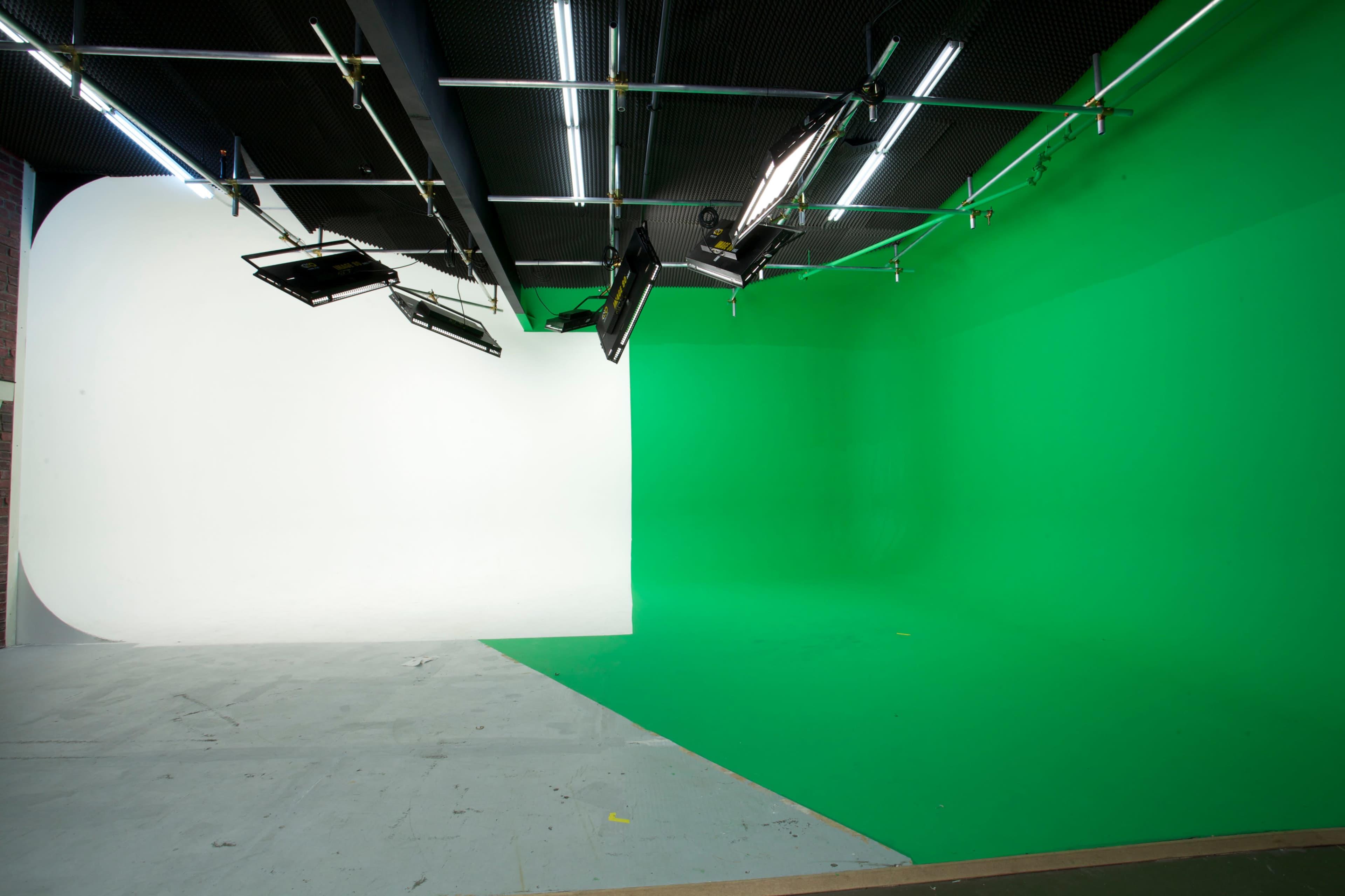 A film studio featuring a white backdrop on the left and a green screen on the right, with overhead lighting equipment positioned above.