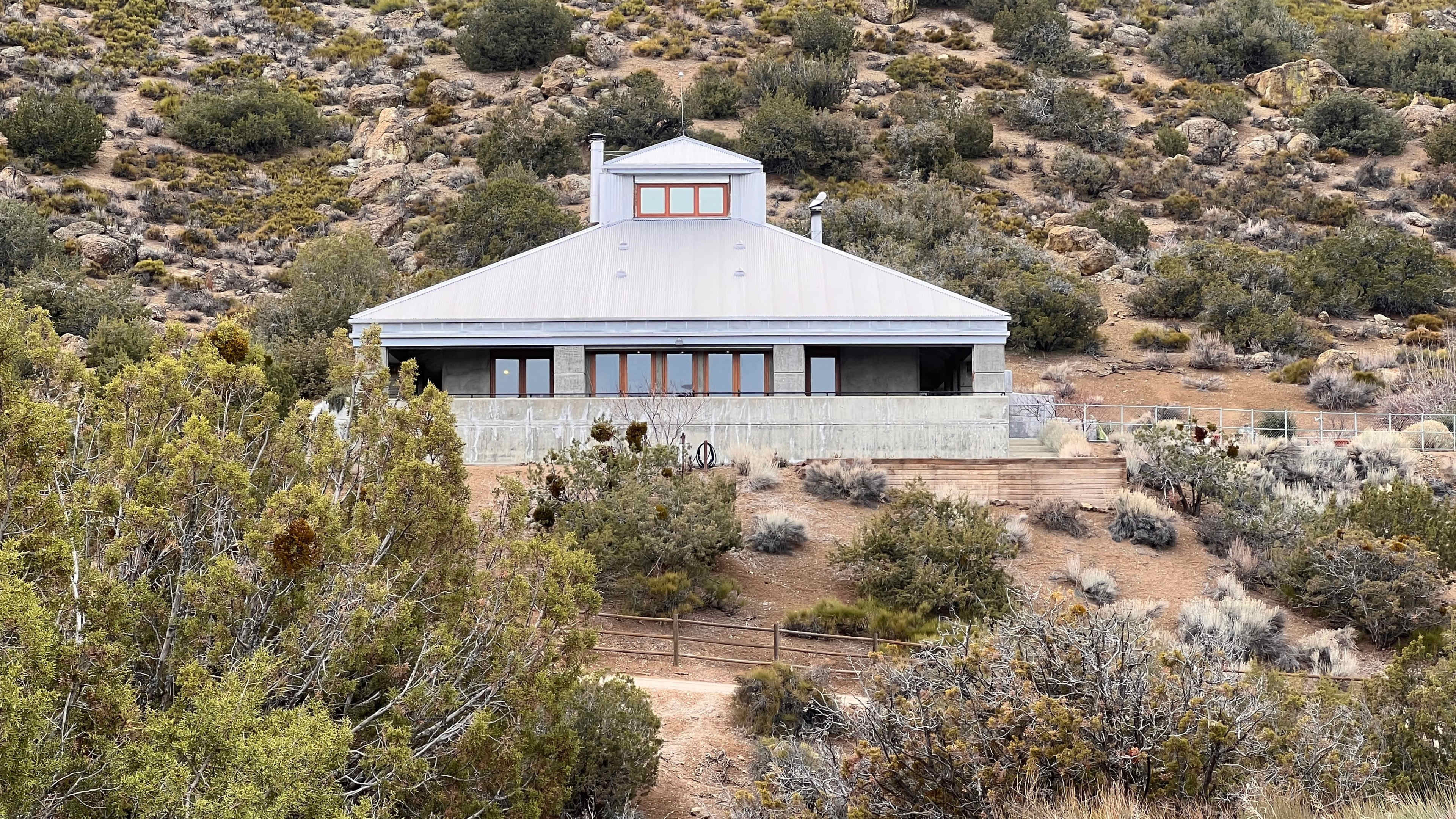 A large, modern house situated on a hillside surrounded by sparse vegetation.