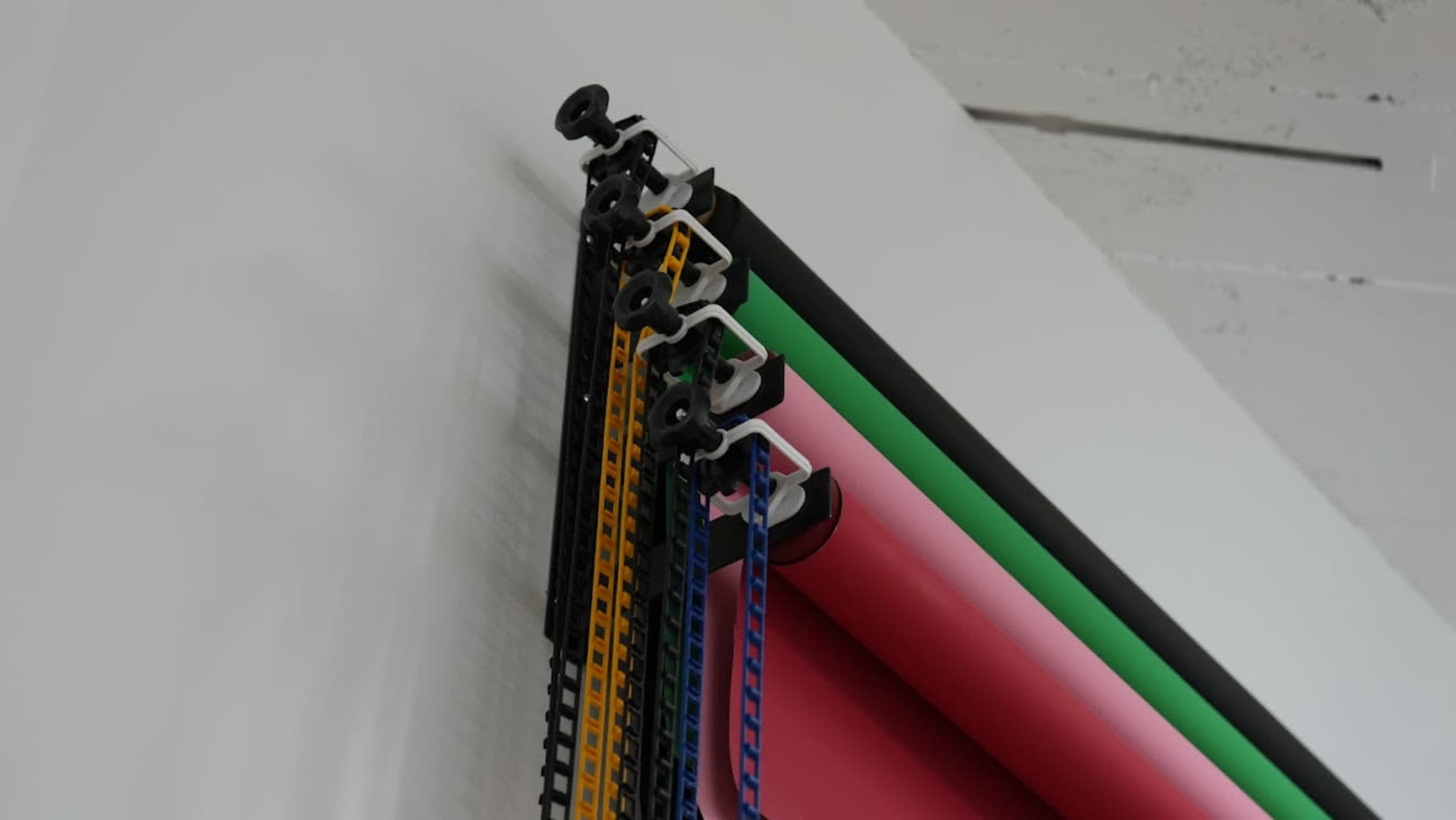 The image shows a collection of rolled backdrop papers in various colors, secured by clips at the top and hanging vertically against a wall.