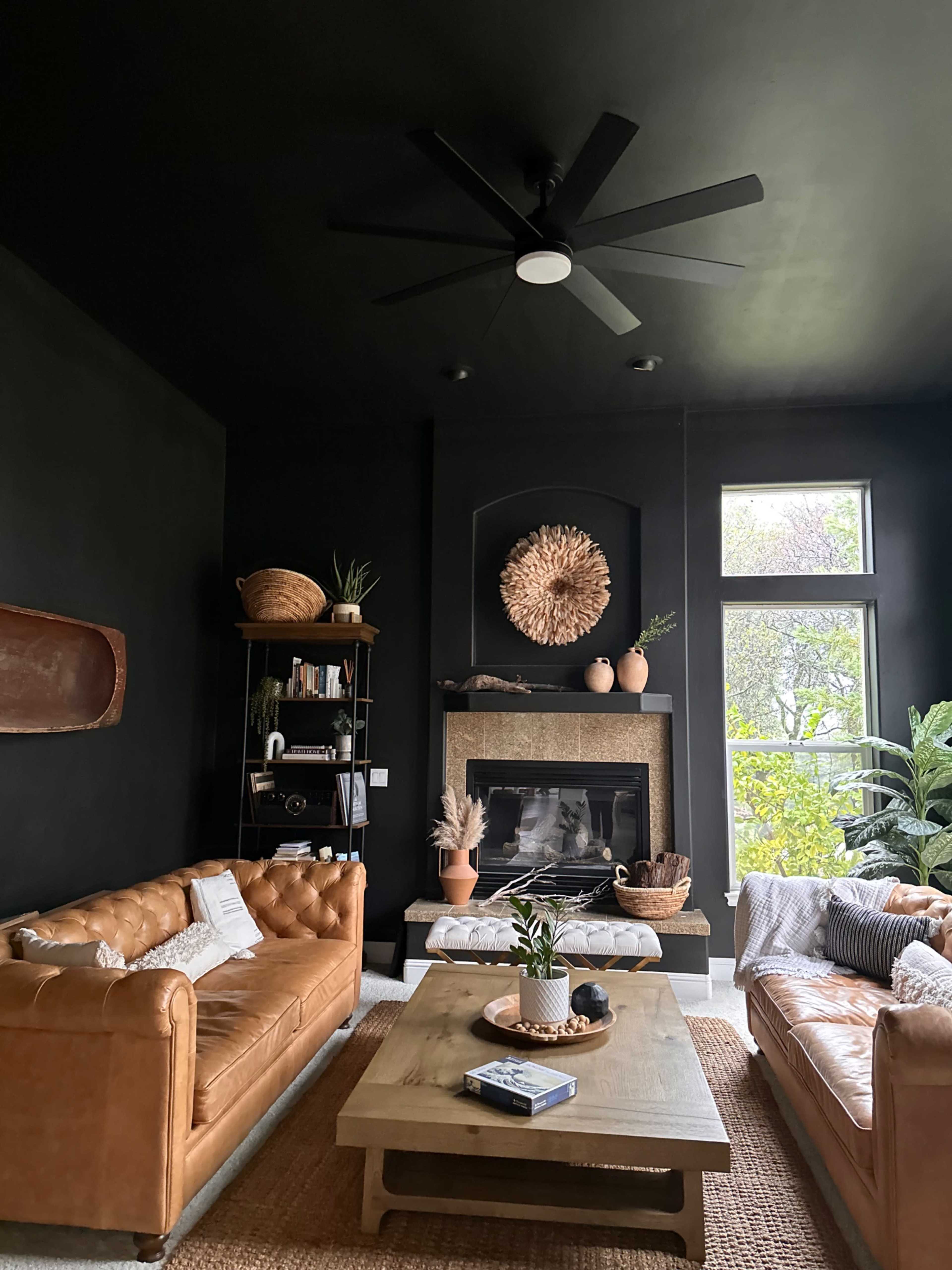 A modern living room with black walls, leather sofas, a wooden coffee table, and a fireplace surrounded by decorative elements.