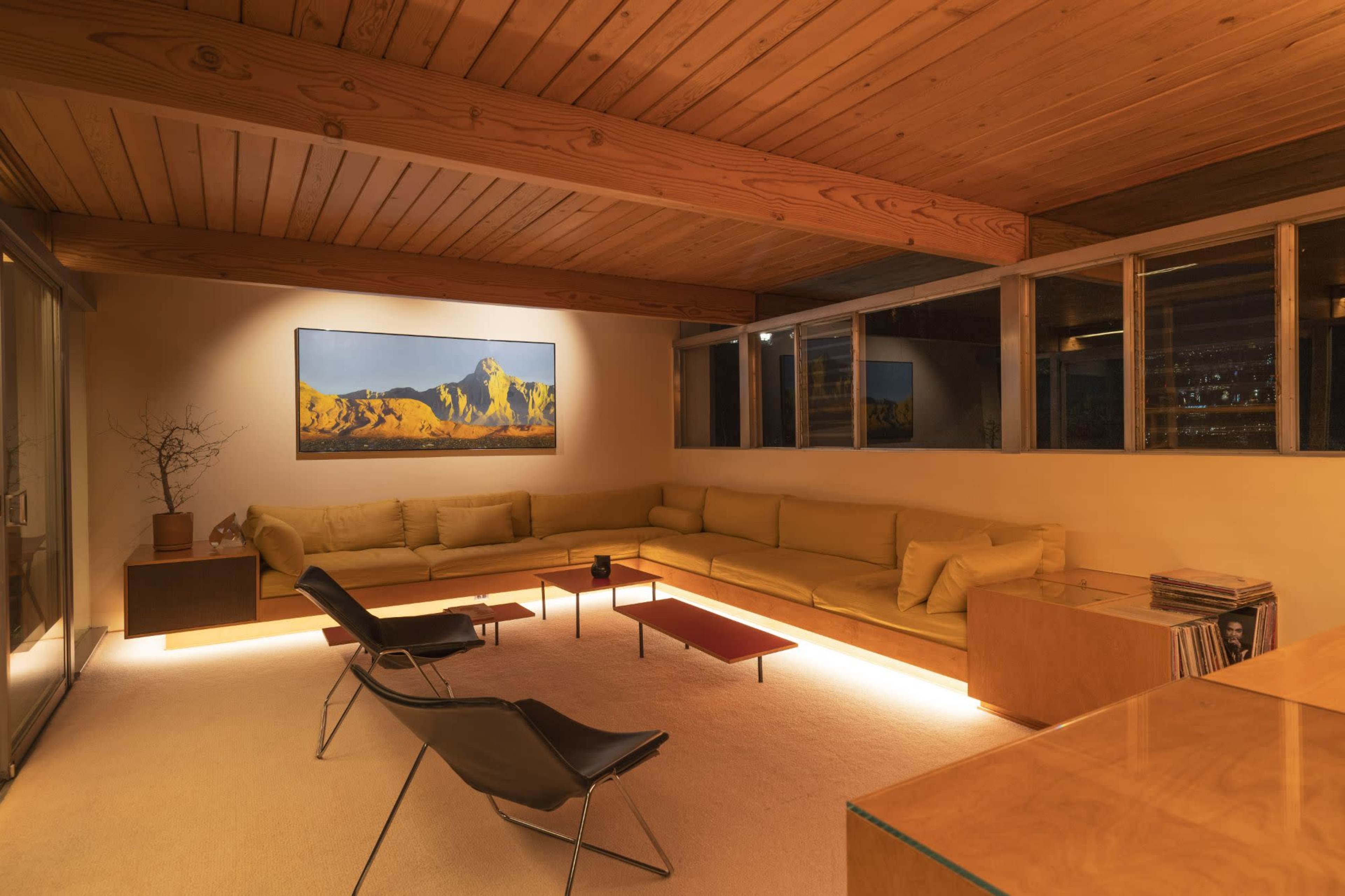 The image features a modern living room with a large sectional sofa, two black chairs, wooden beams on the ceiling, and a landscape painting on the wall.