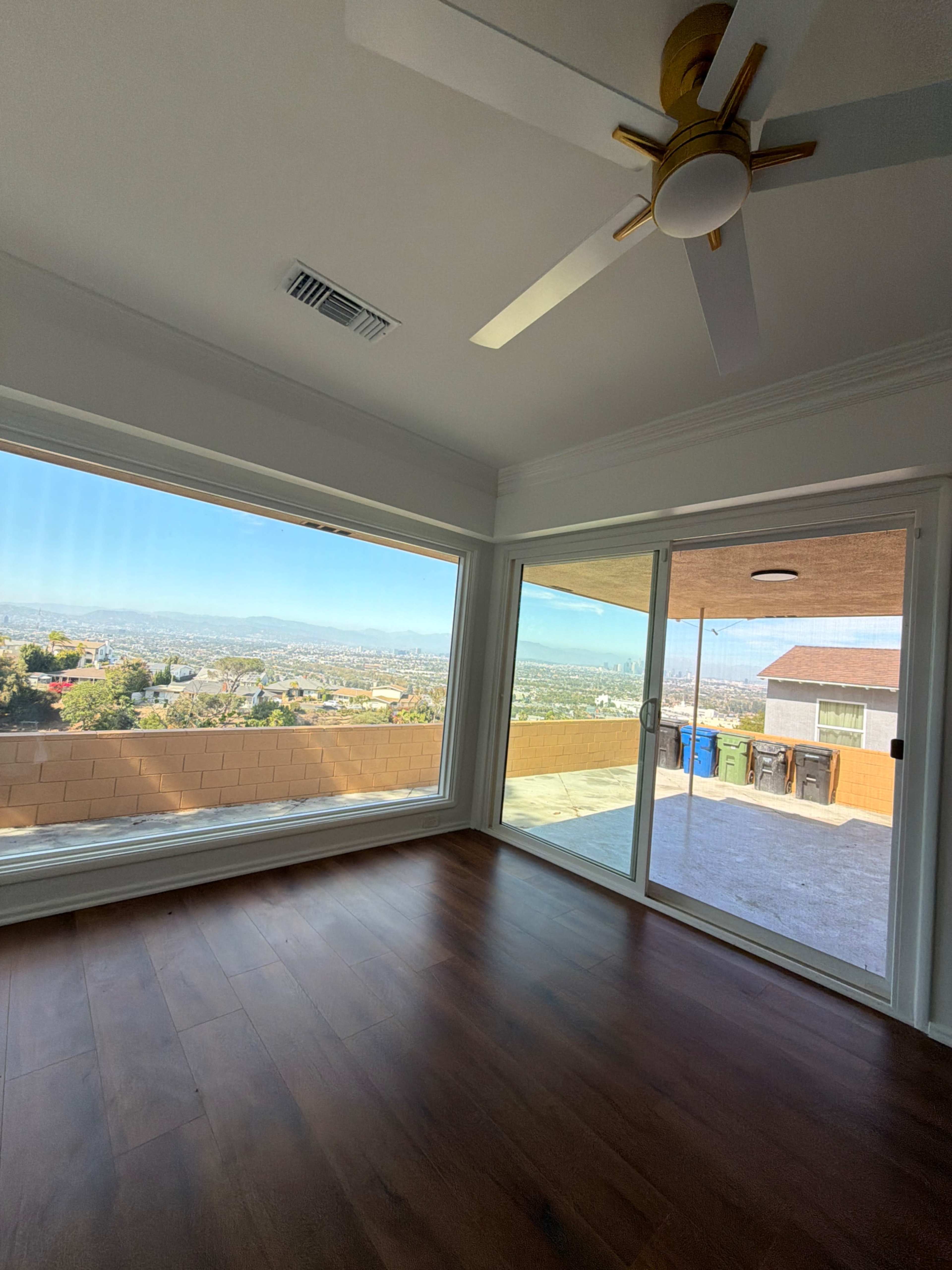 The image shows a spacious, empty room with large windows offering a panoramic view of a cityscape and mountains in the distance.