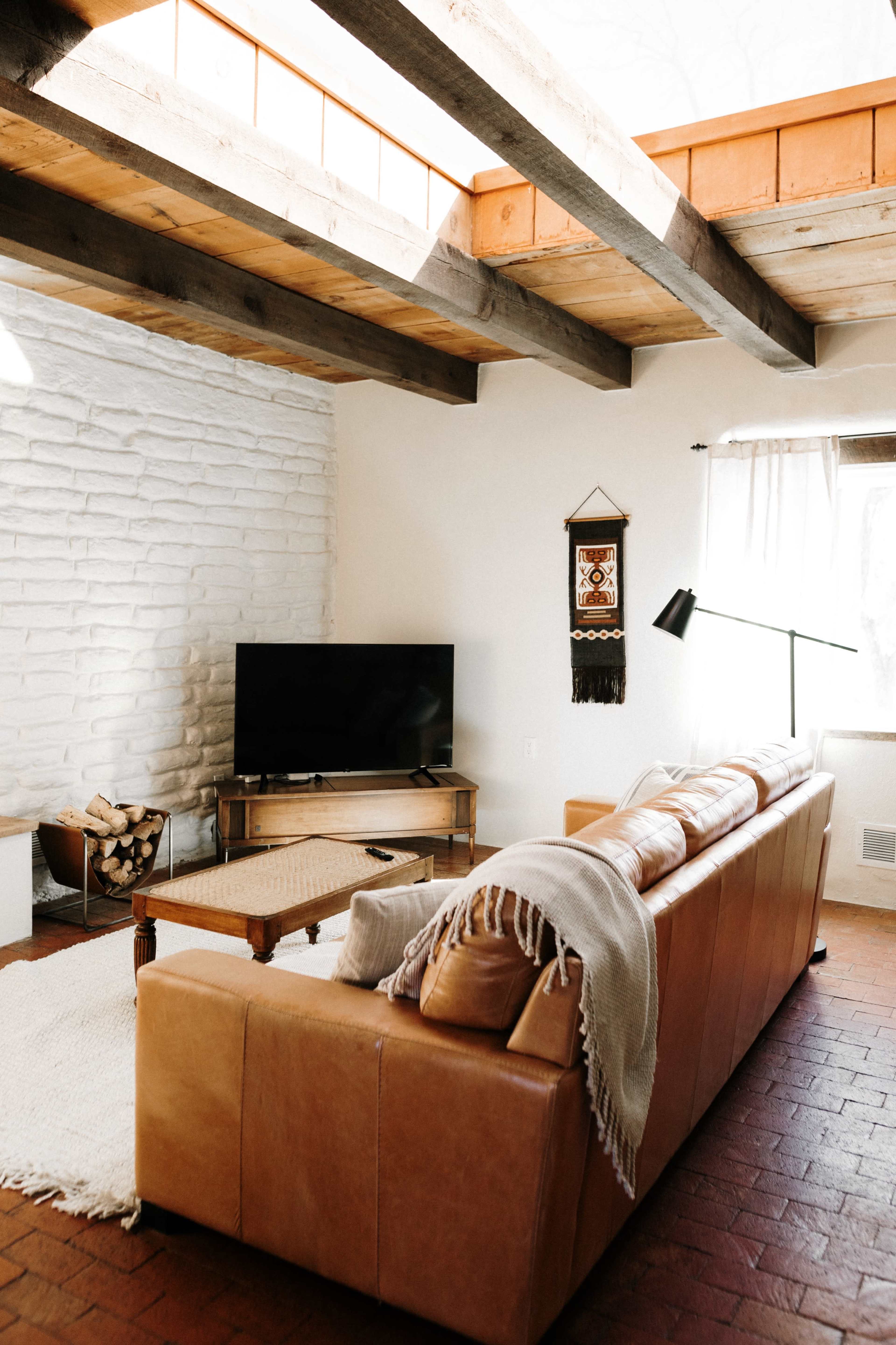 A cozy living room featuring a leather sofa, a wooden coffee table, a television, and a large window allowing natural light to enter.