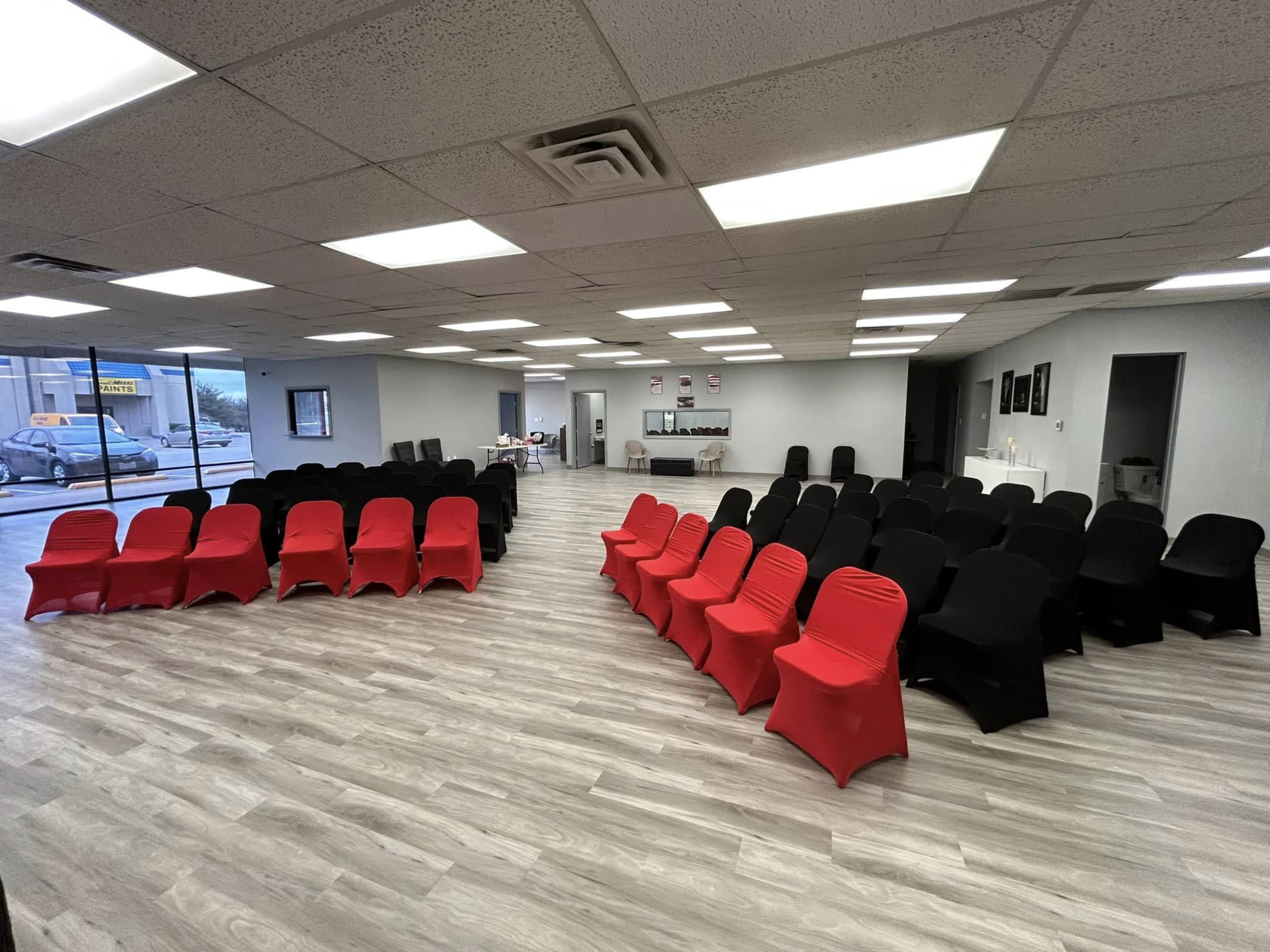 A spacious seminar room features rows of black and red chairs arranged in a circular pattern on a light-colored floor.