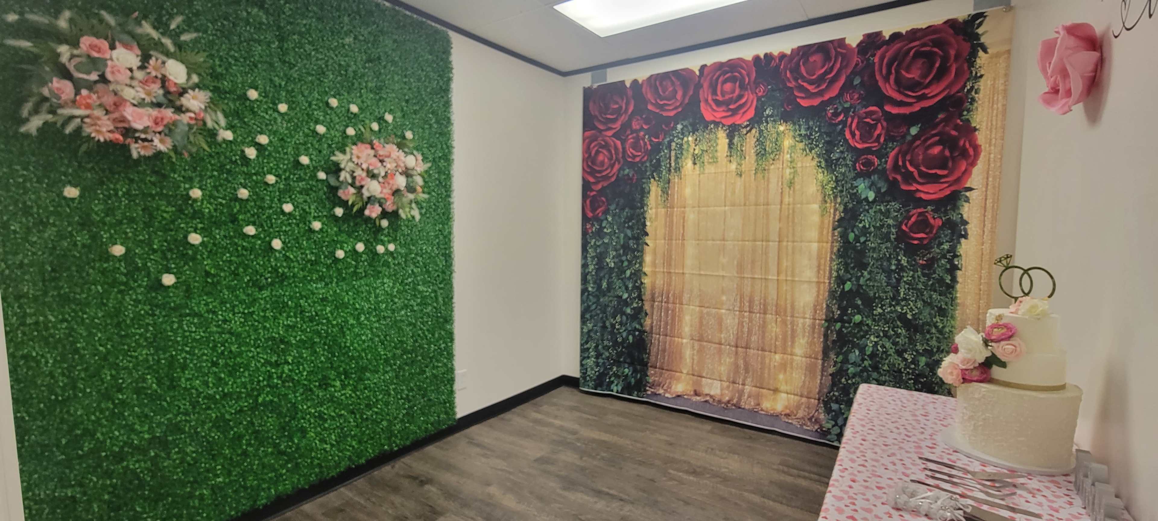 A decorated room with a green grass wall on one side, adorned with floral decorations, and a wall featuring large red roses and a golden curtain backdrop.