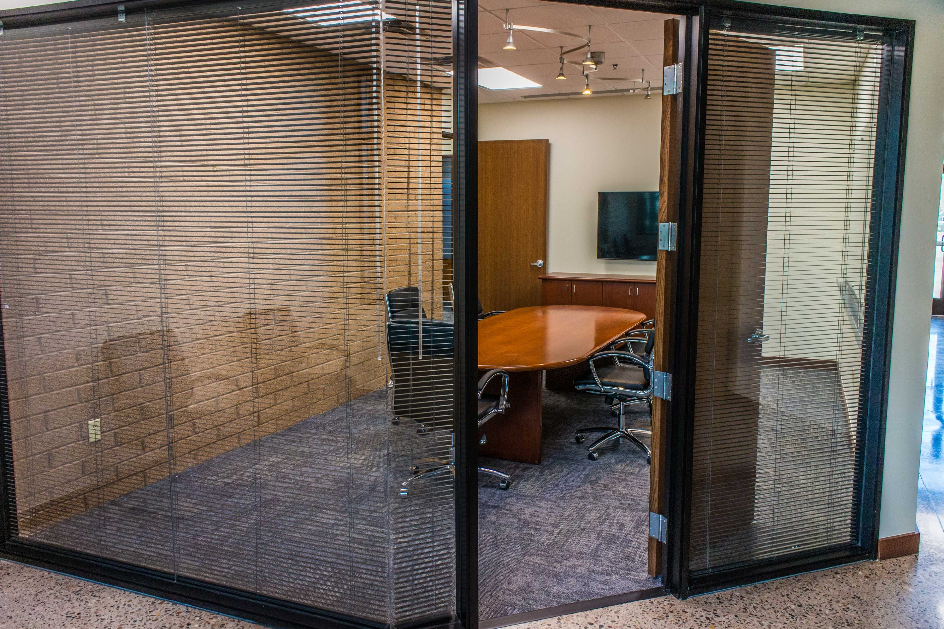 A glass-walled conference room features a wooden table surrounded by ergonomic chairs.