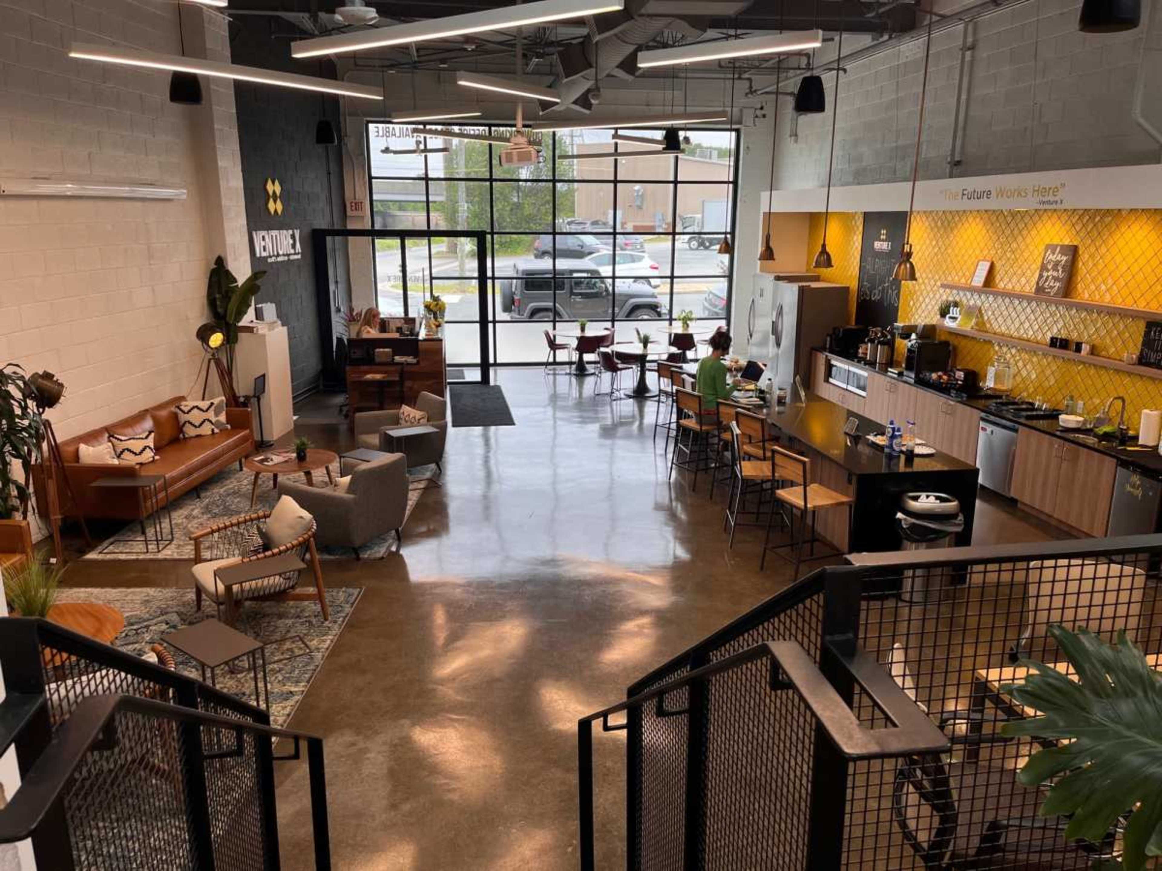 A modern co-working space with a blend of seating areas, a café-style counter, and large windows allowing natural light.