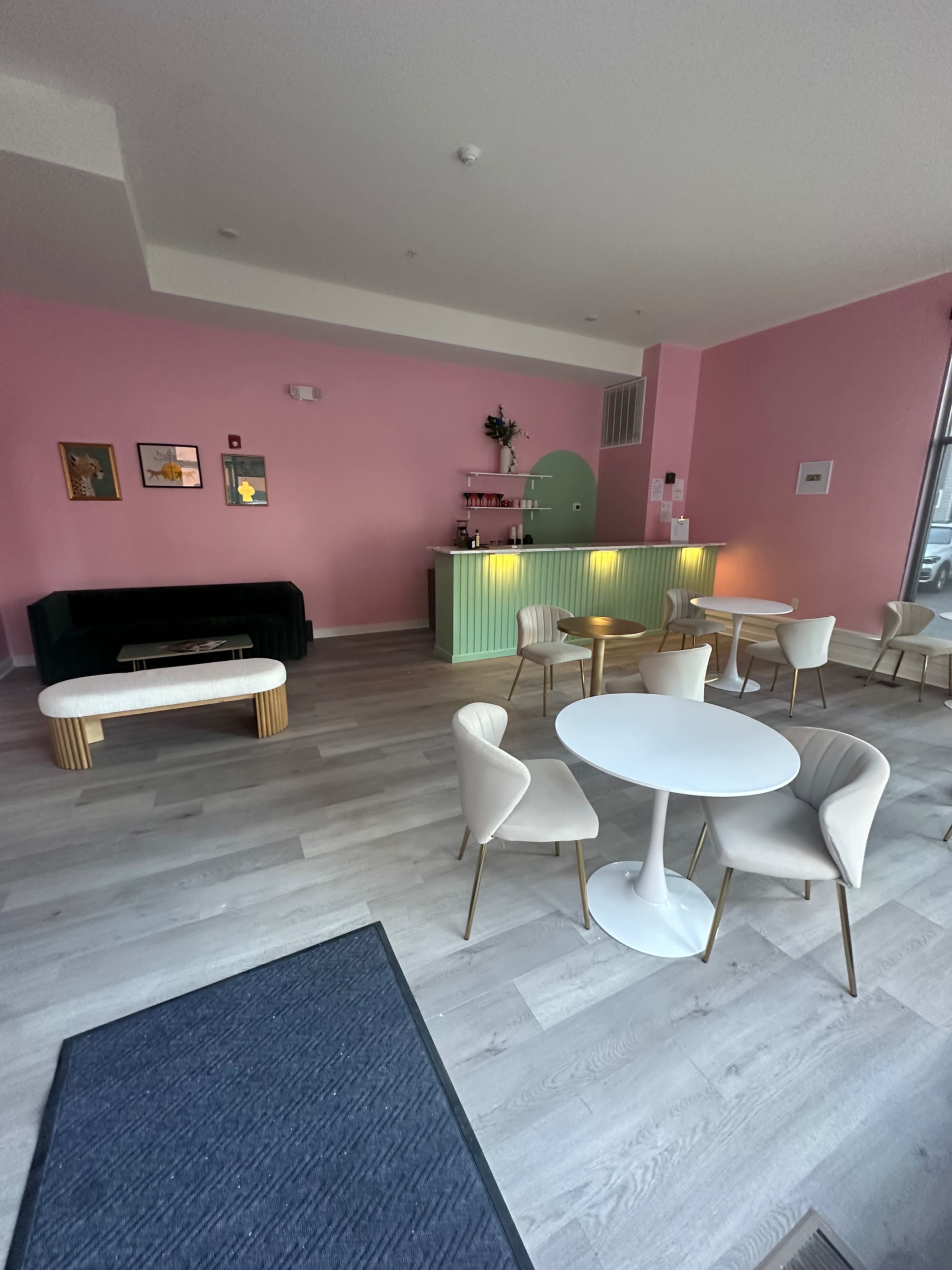 A modern café interior with pink walls, a green counter, and white tables and chairs.