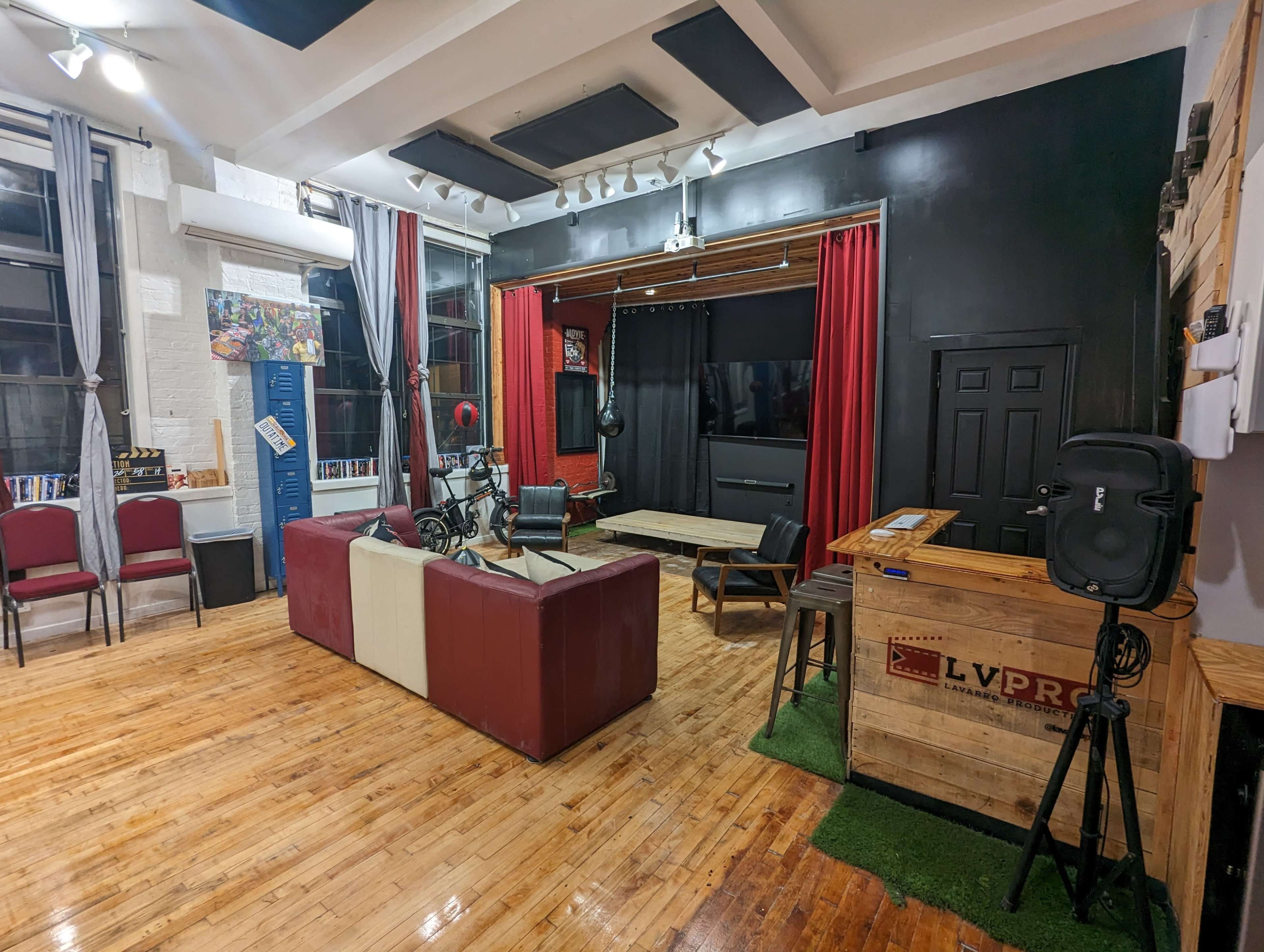 A spacious studio setting with a mix of red velvet curtains, a large screen, wooden furniture, and a combination of seating areas, including a couch and chairs.