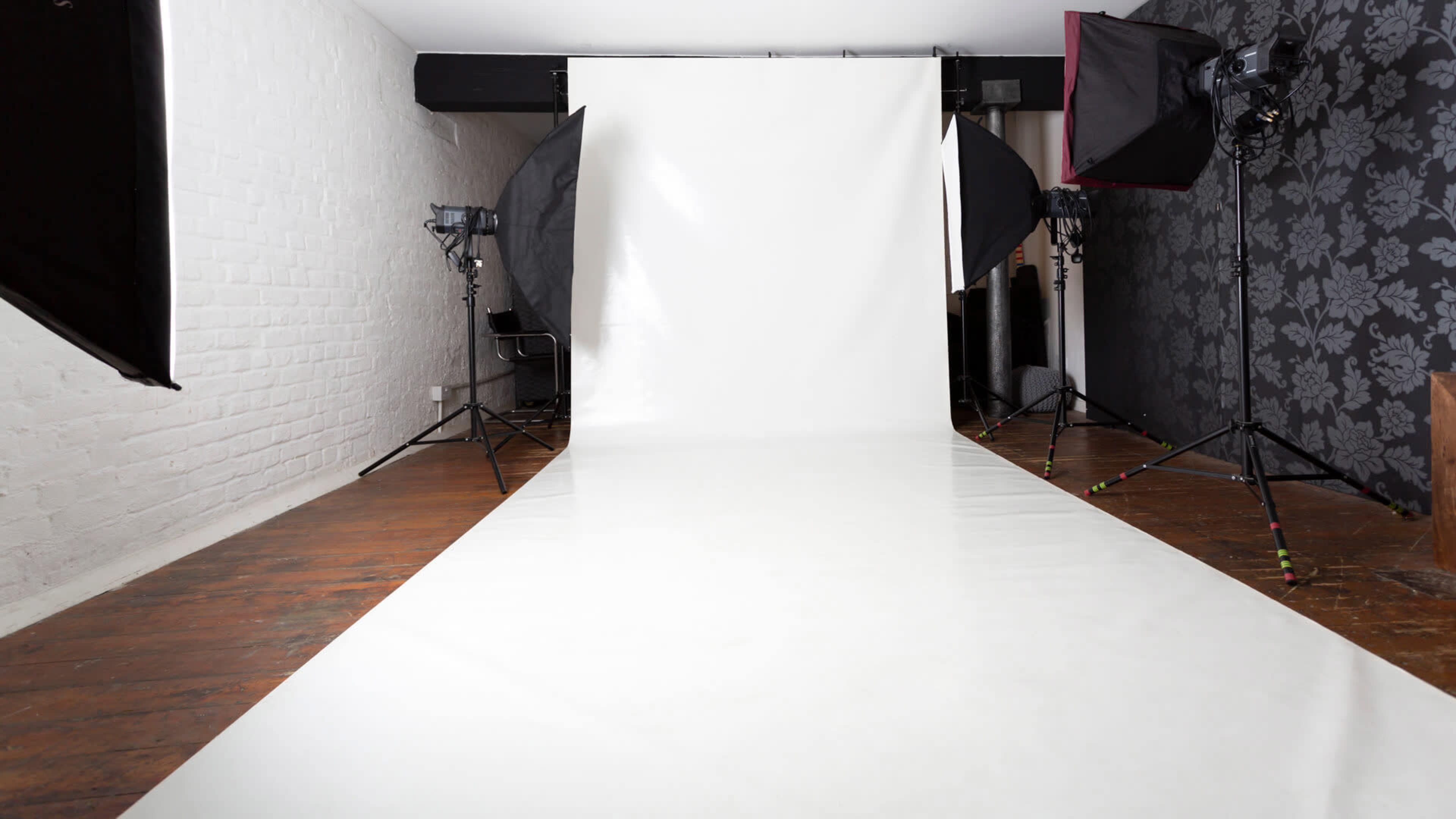 A photography studio with a white backdrop, a roll of white floor covering, and lighting equipment set up on either side.
