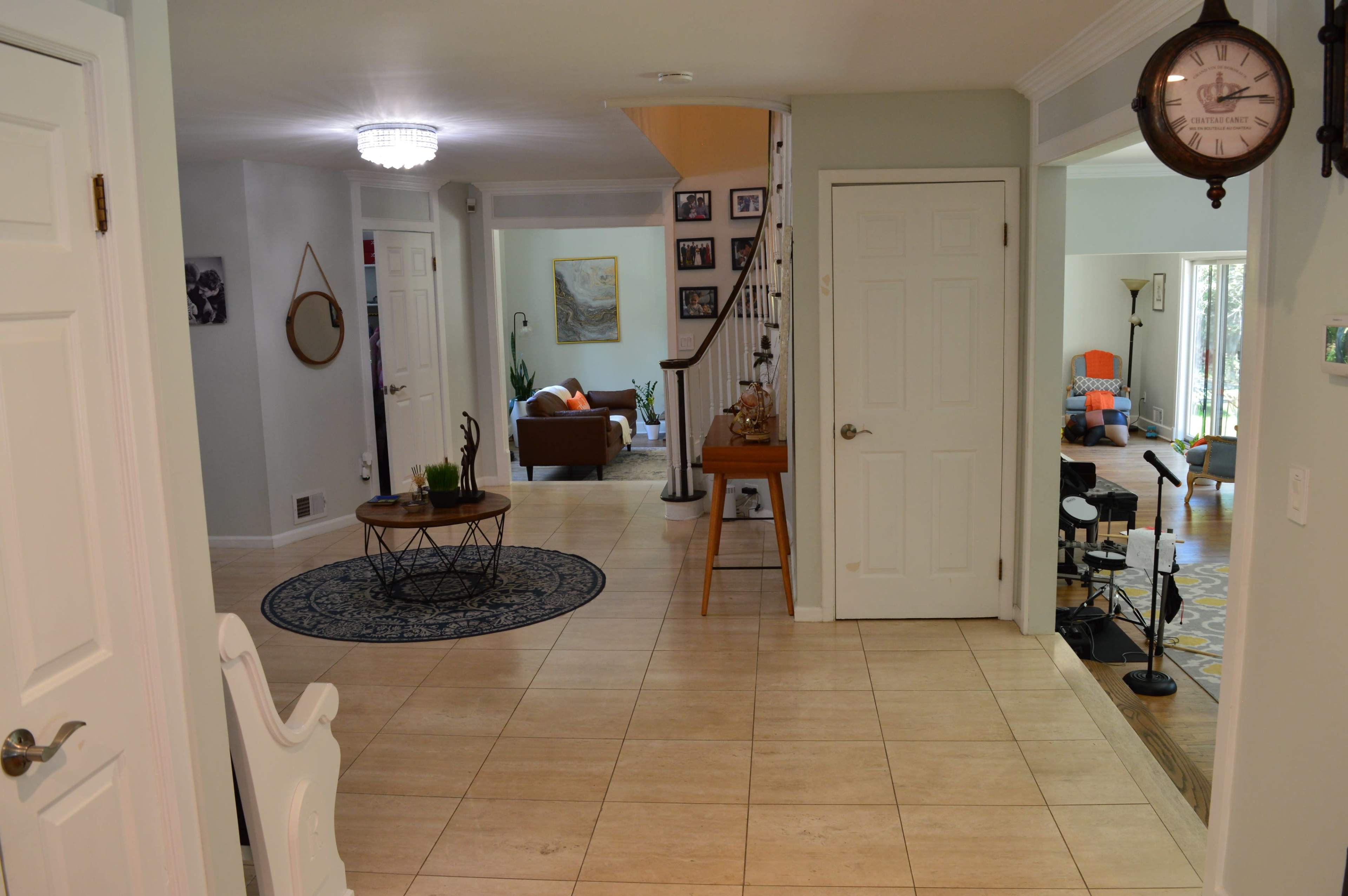 The image shows a large, open foyer with tiled flooring, leading into a living area visible in the background, and a staircase on the right.