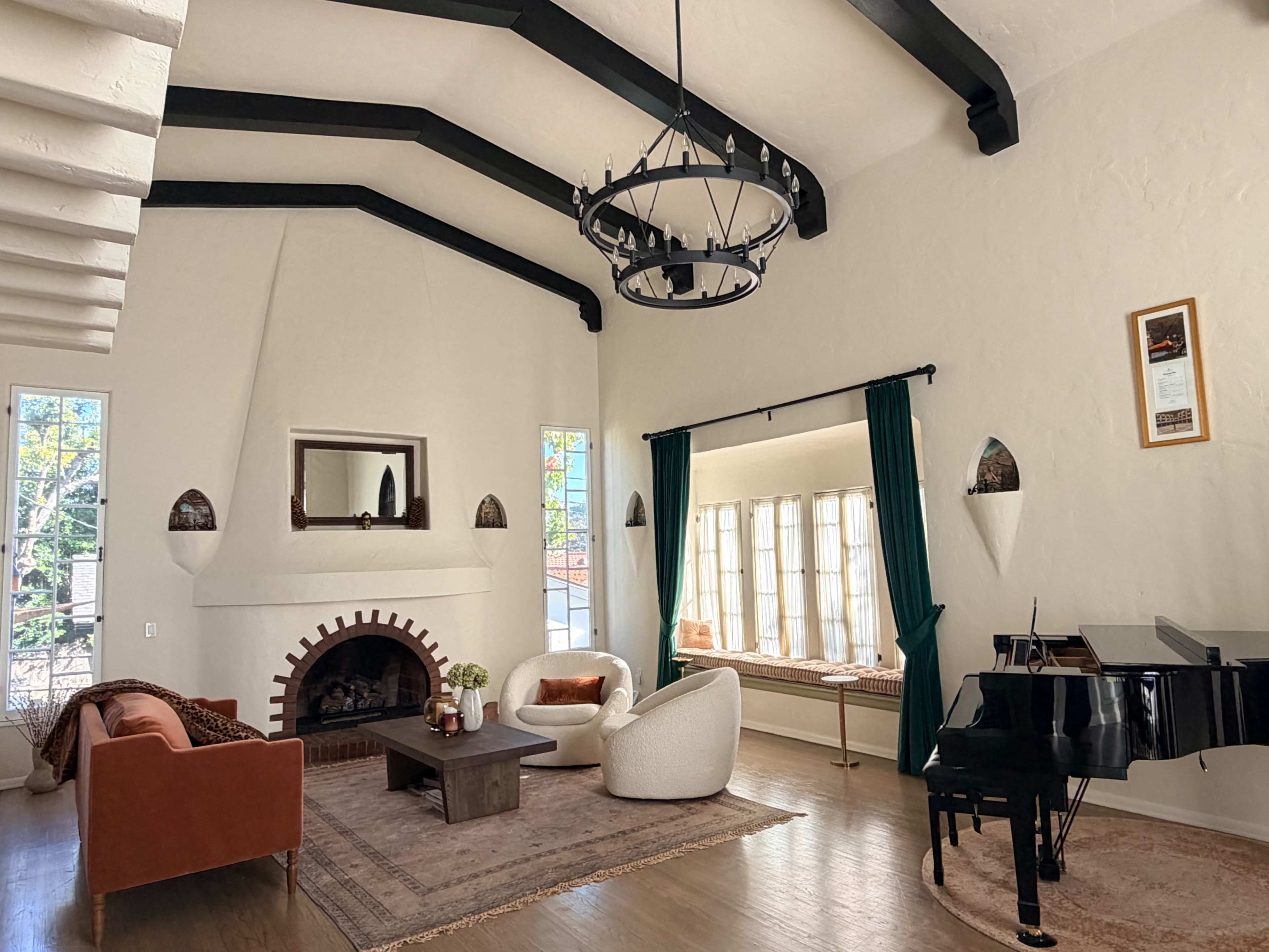 The living room features high ceilings with exposed beams, a large fireplace, and a grand piano beside a windowed sitting area.