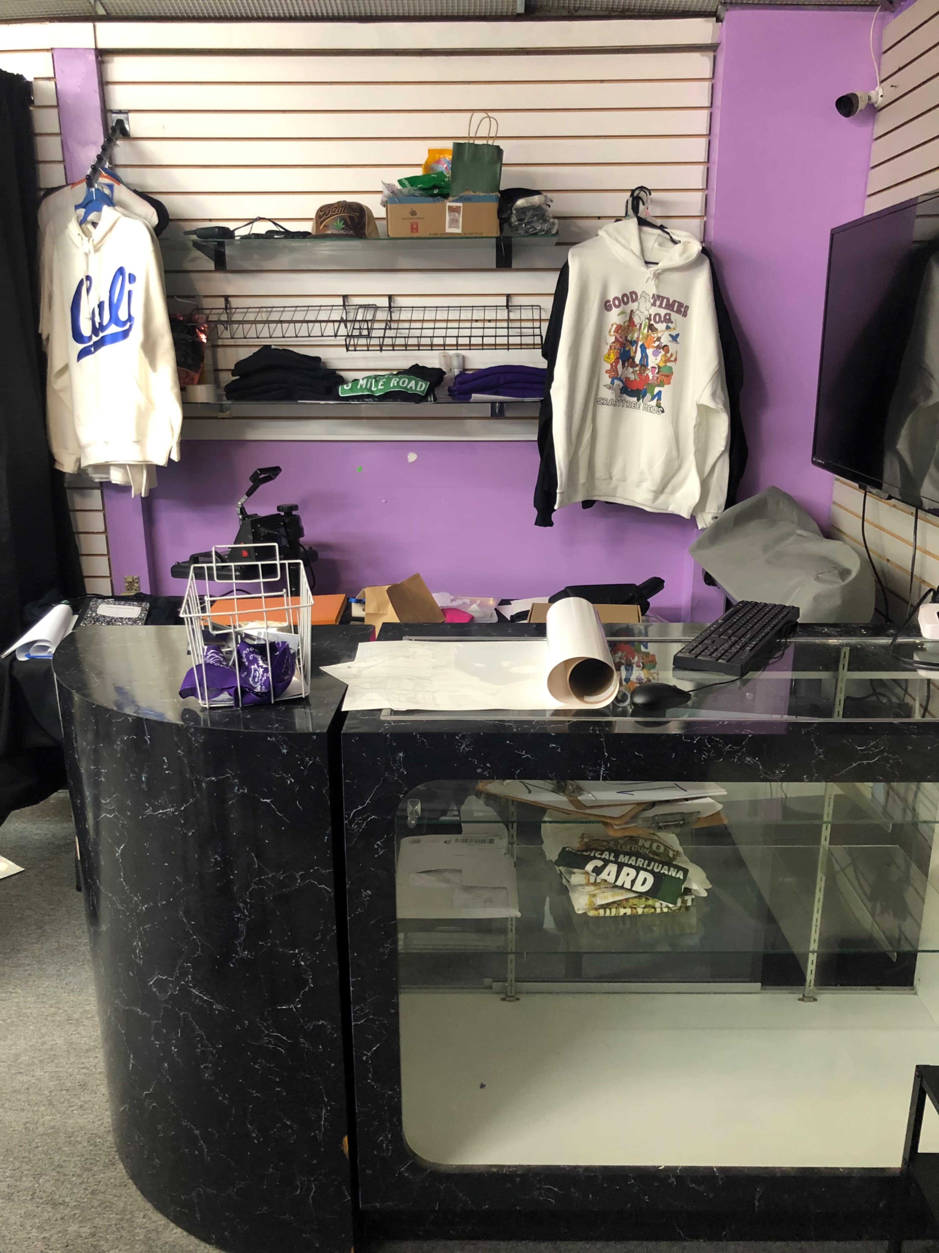 A retail display area with a curved counter, shelves containing clothing items, and a television mounted on the wall.