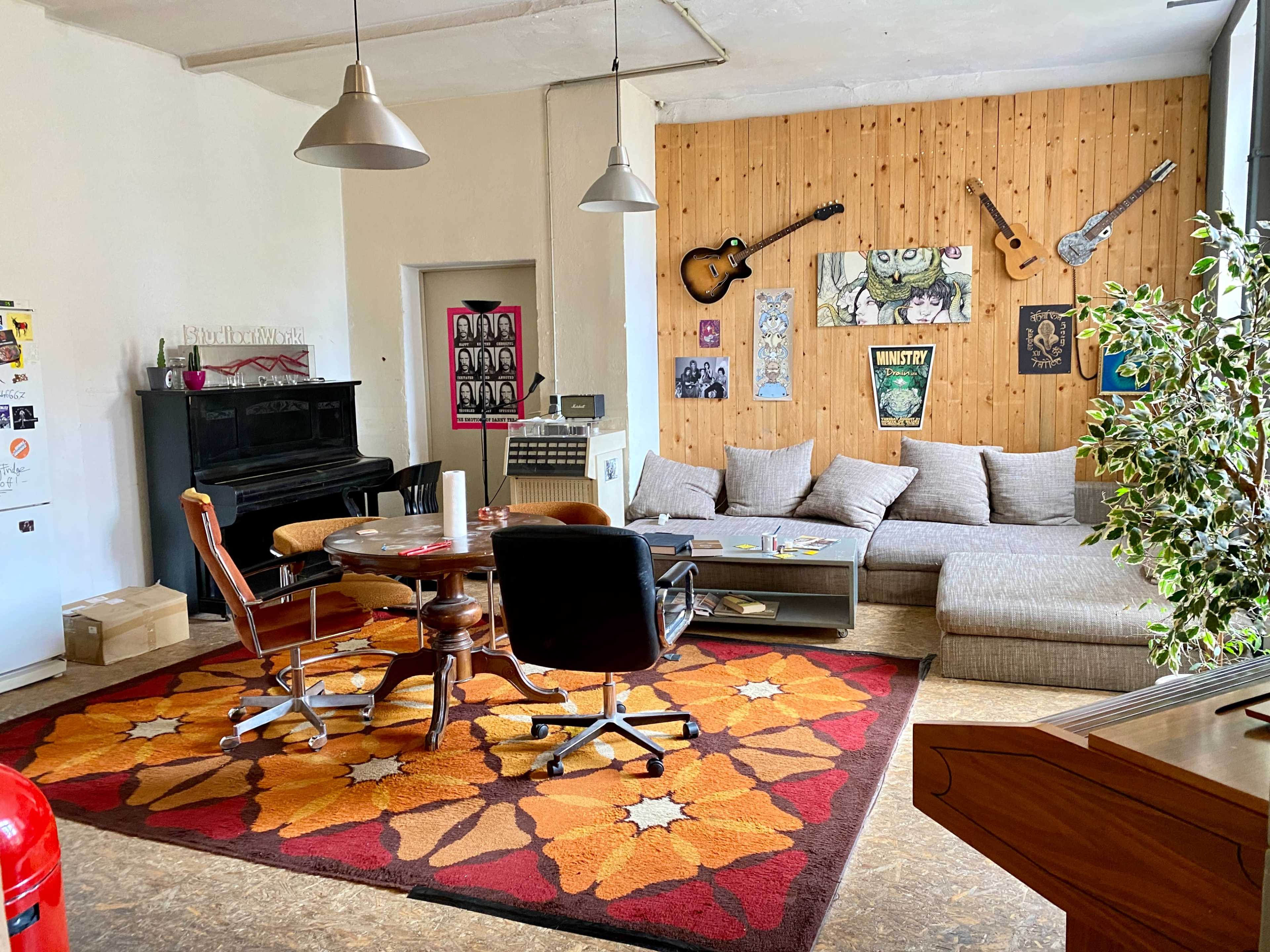 A spacious living room with a mix of furniture, including a sofa, armchairs, a coffee table, and a piano, surrounded by wooden walls and decorated with various artworks.
