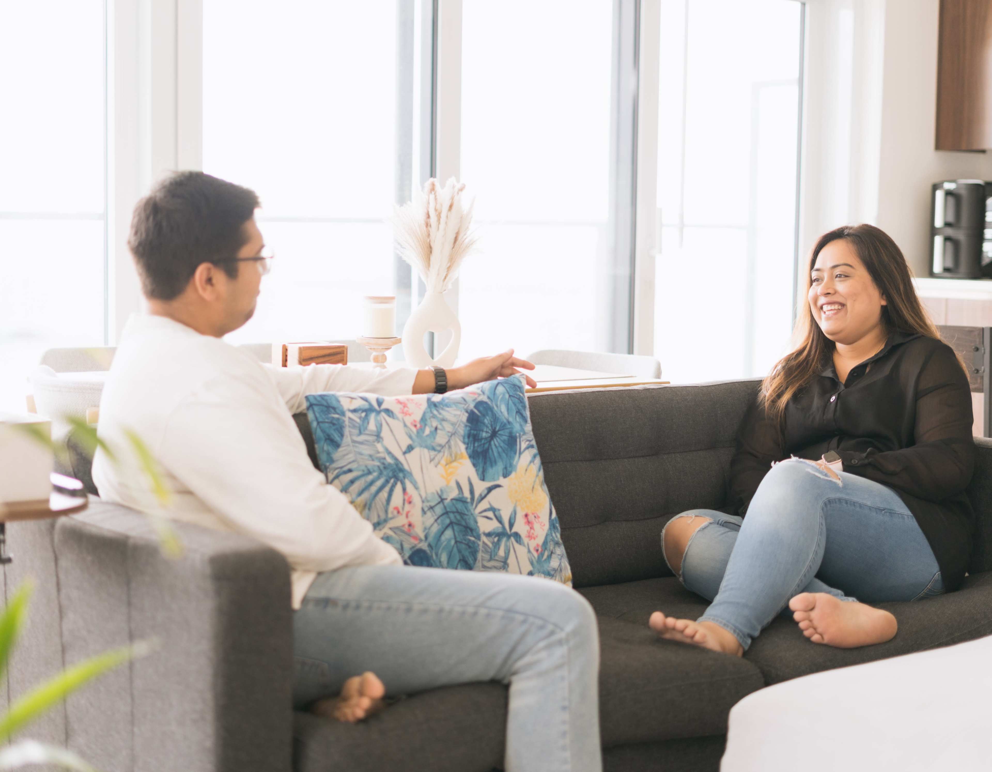 A man and a woman are seated on a gray sofa in a modern living room, engaged in conversation.