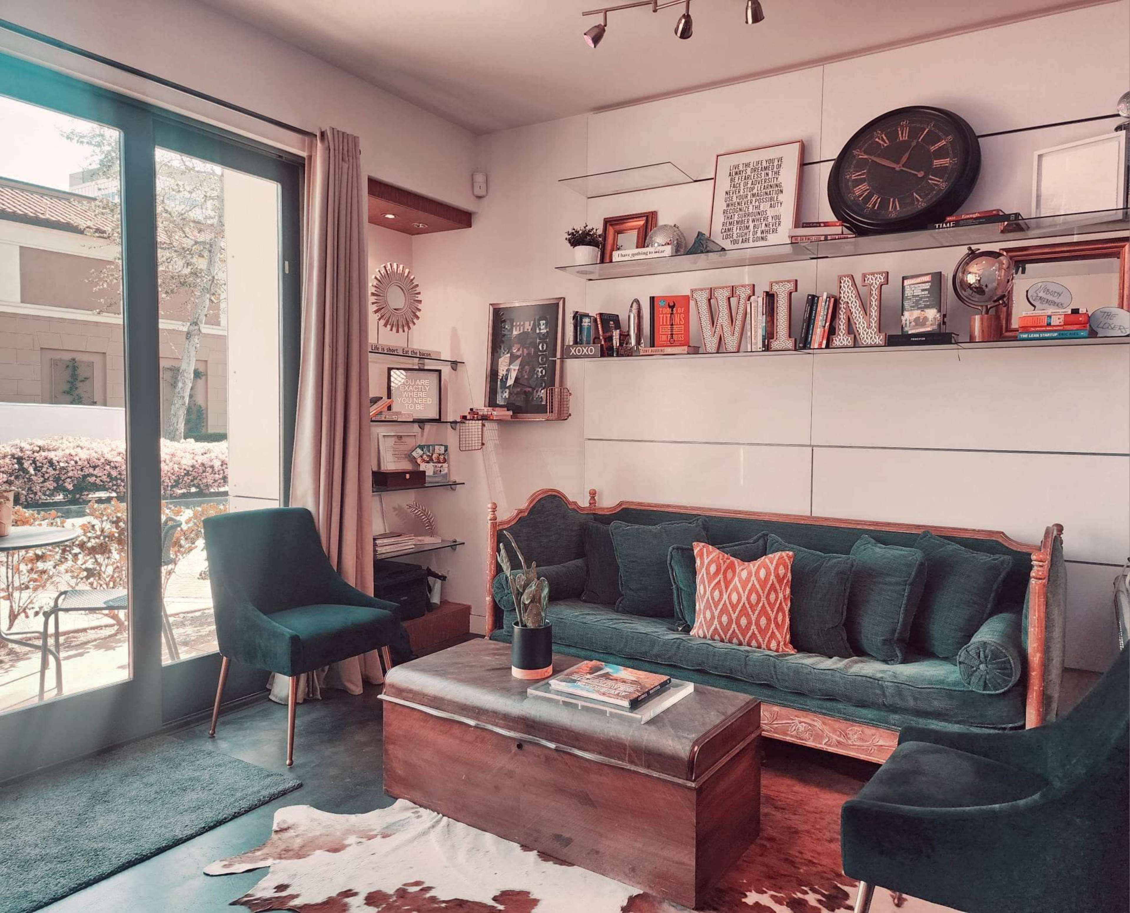 A modern living room featuring a green velvet sofa, a wooden coffee table, and shelves adorned with decorative items and a clock.