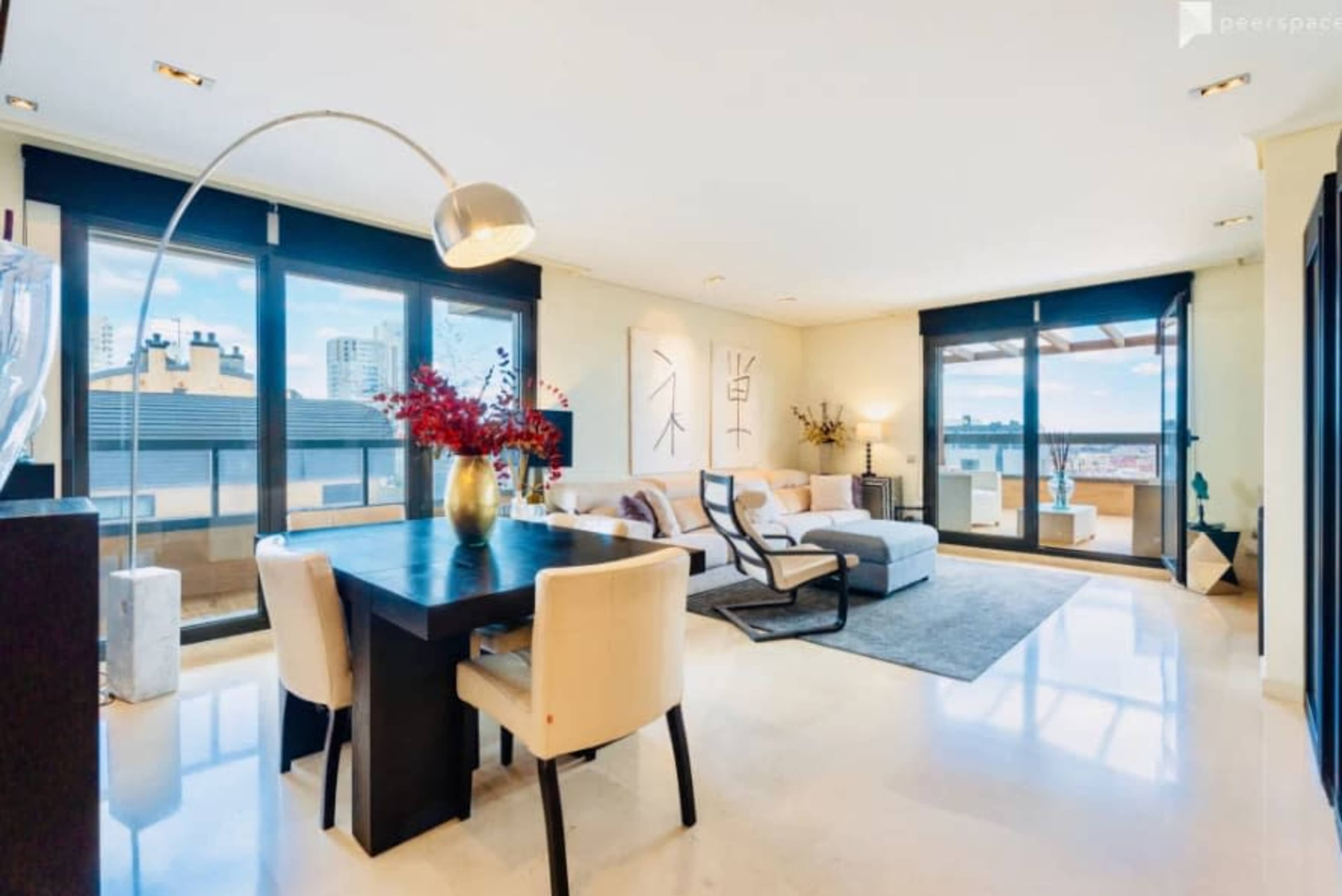 The image shows a modern, well-lit living room with large windows, a dining table, and a comfortable seating area featuring a sectional sofa.