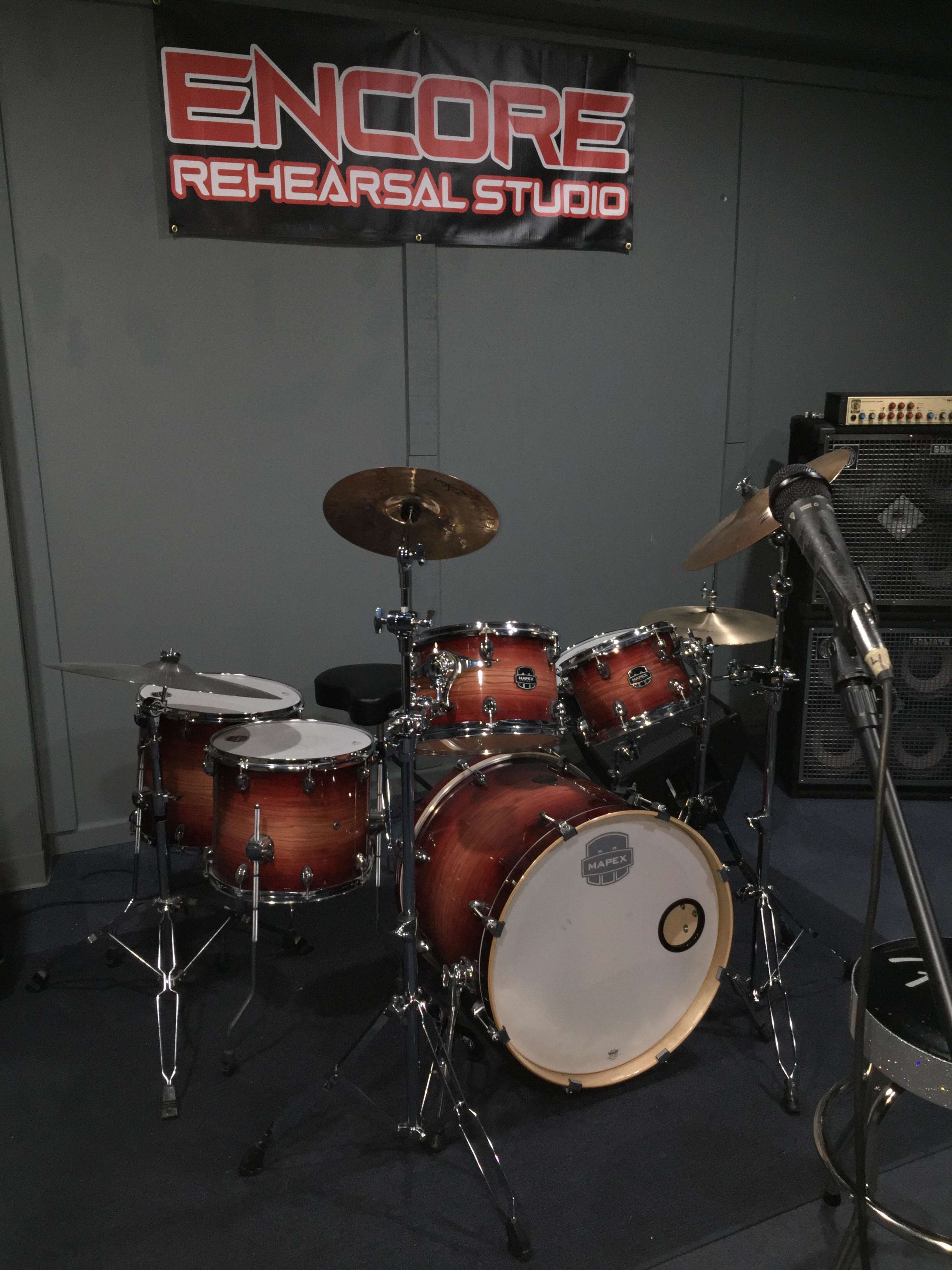 A drum set in a rehearsal studio with a banner reading "ENCORE REHEARSAL STUDIO" in the background.