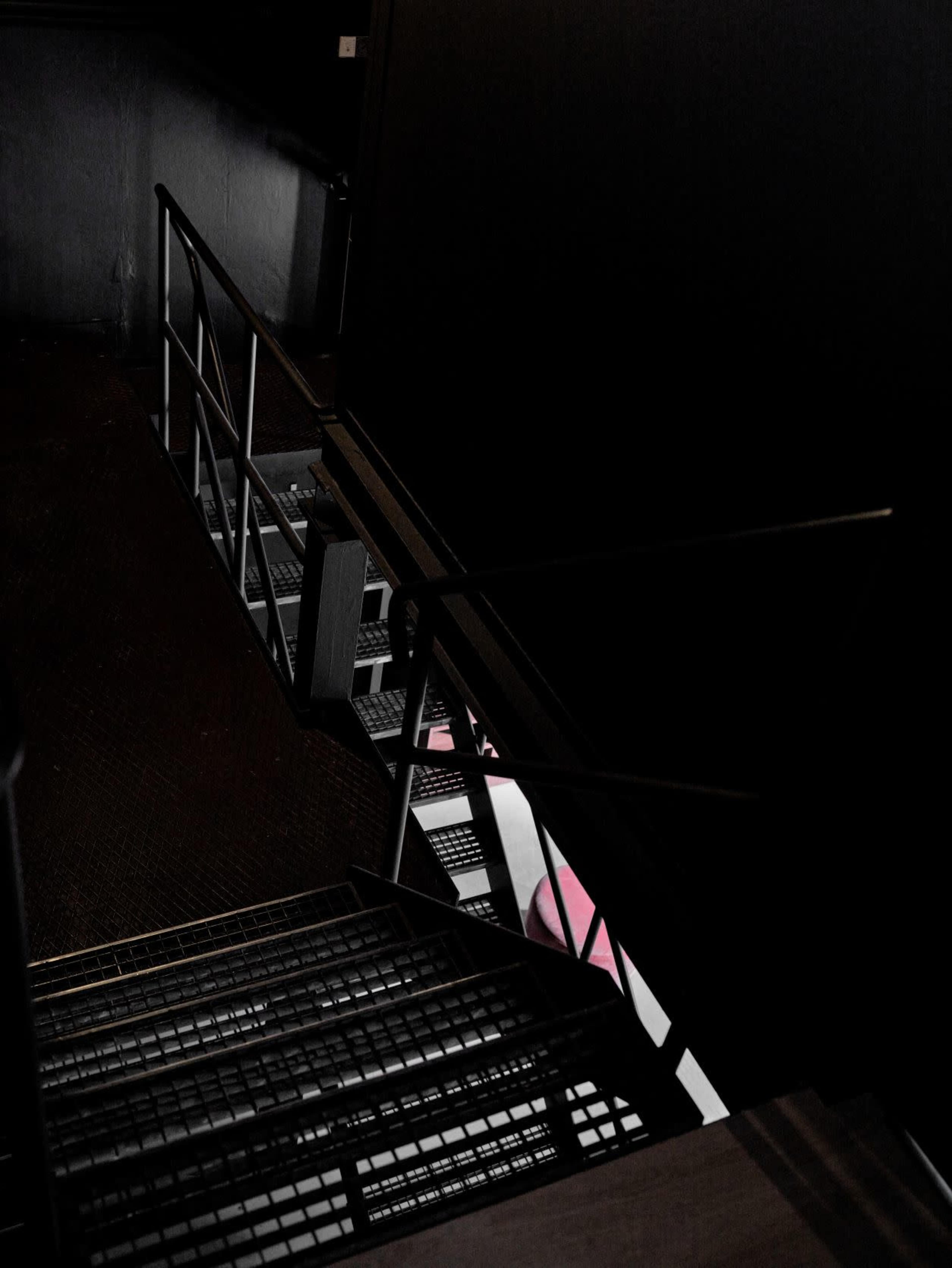 A staircase leads downward in a dark corridor, with metal railings and a textured floor.
