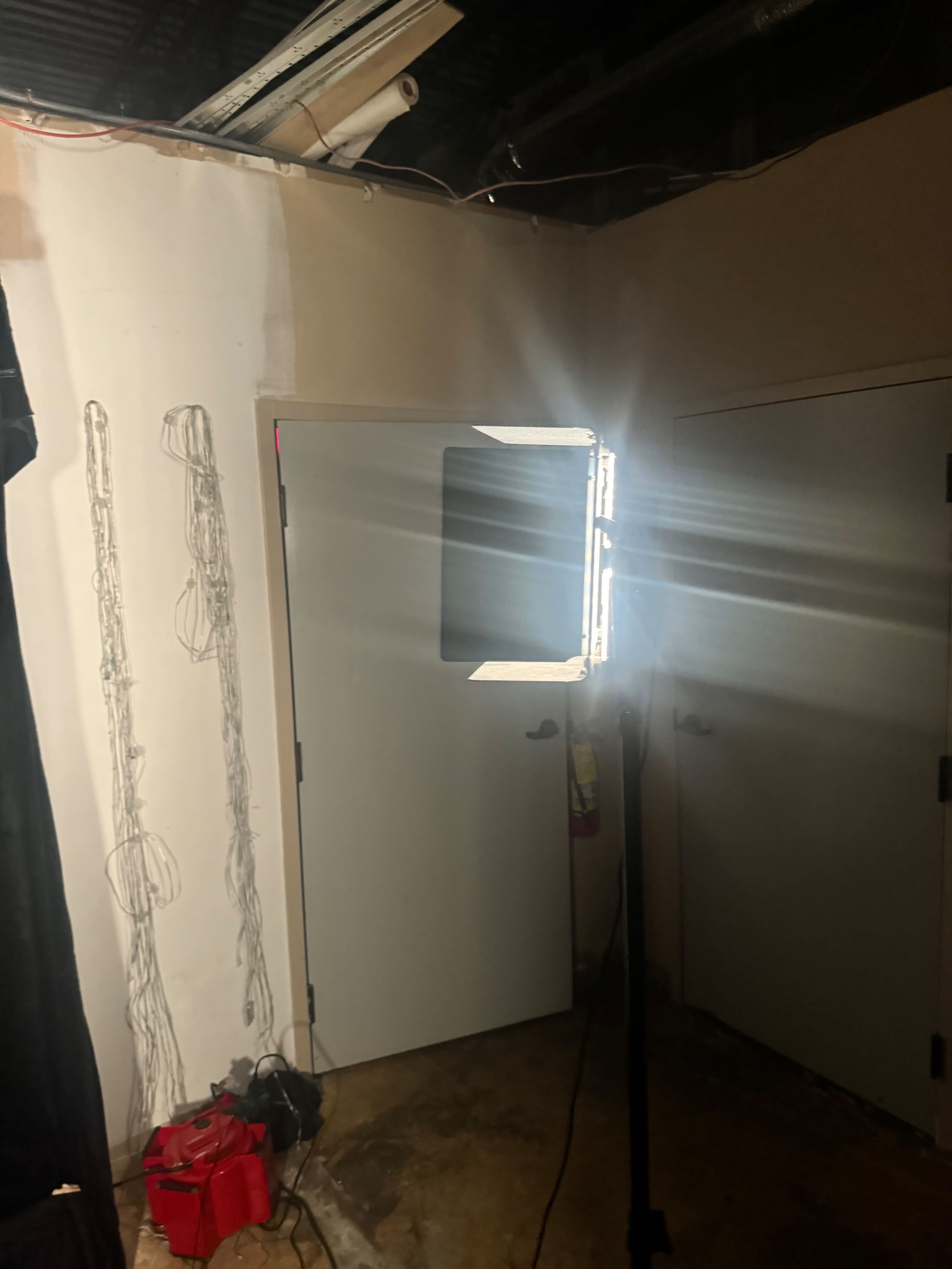 A bright light is positioned in a corner near a closed door, with a faint outline of musical instruments sketched on the wall.